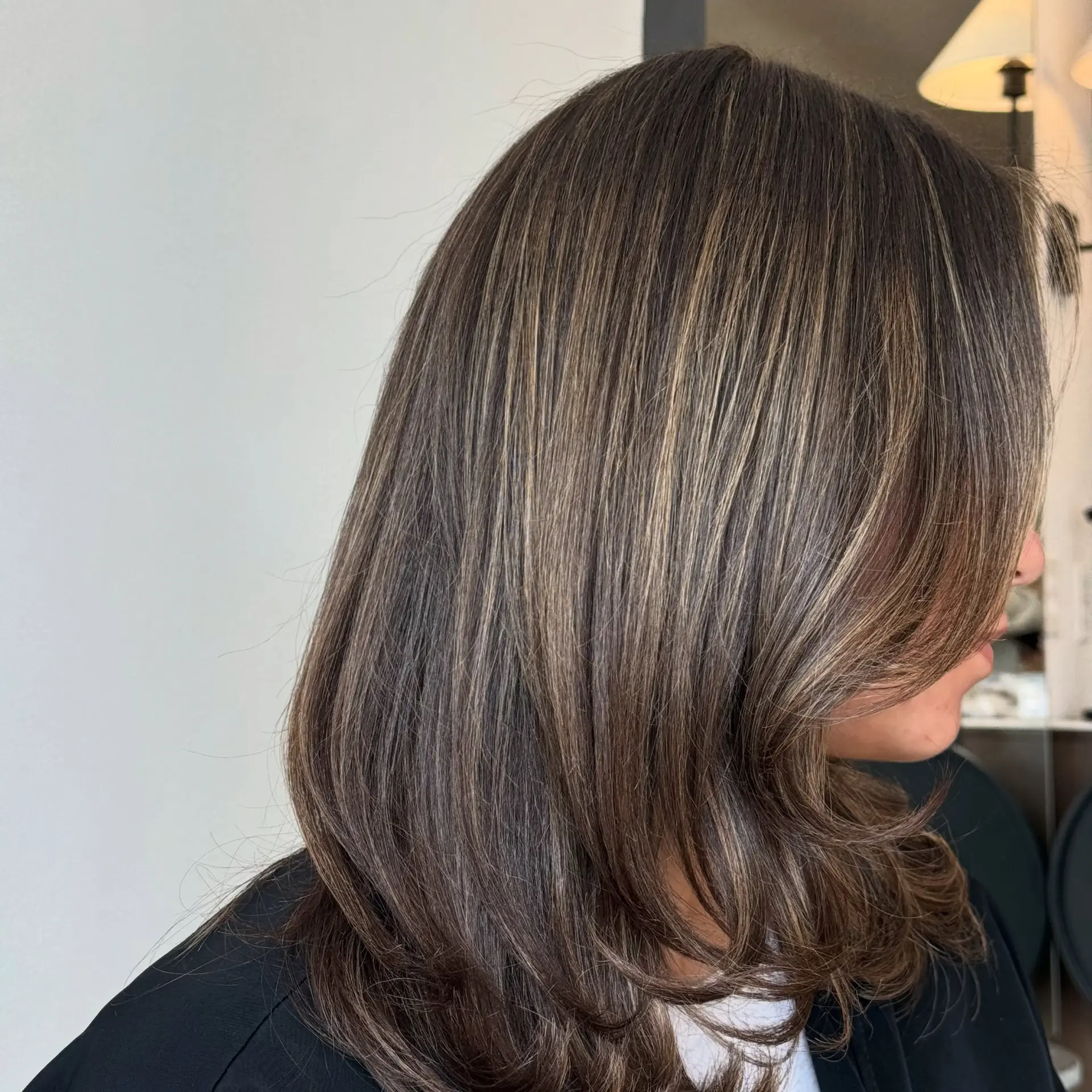 Medium-length brunette hairstyle with fine dimensional highlights and soft, face-framing layers styled with a smooth blowout. 1