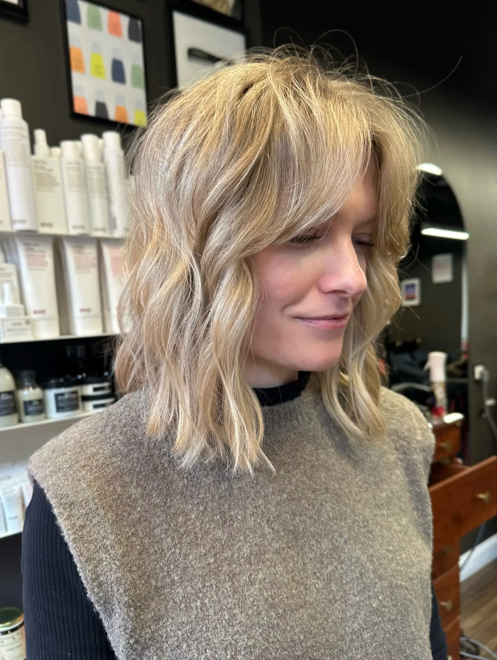 A textured, mid-length blonde lob styled with soft waves and face-framing curtain bangs. 1