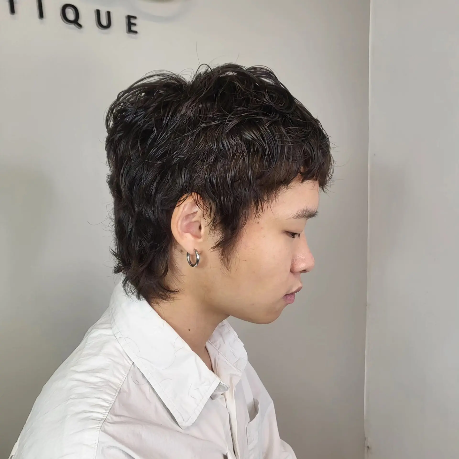 A textured short shaggy cut featuring soft permed waves and slight length along the nape. 1