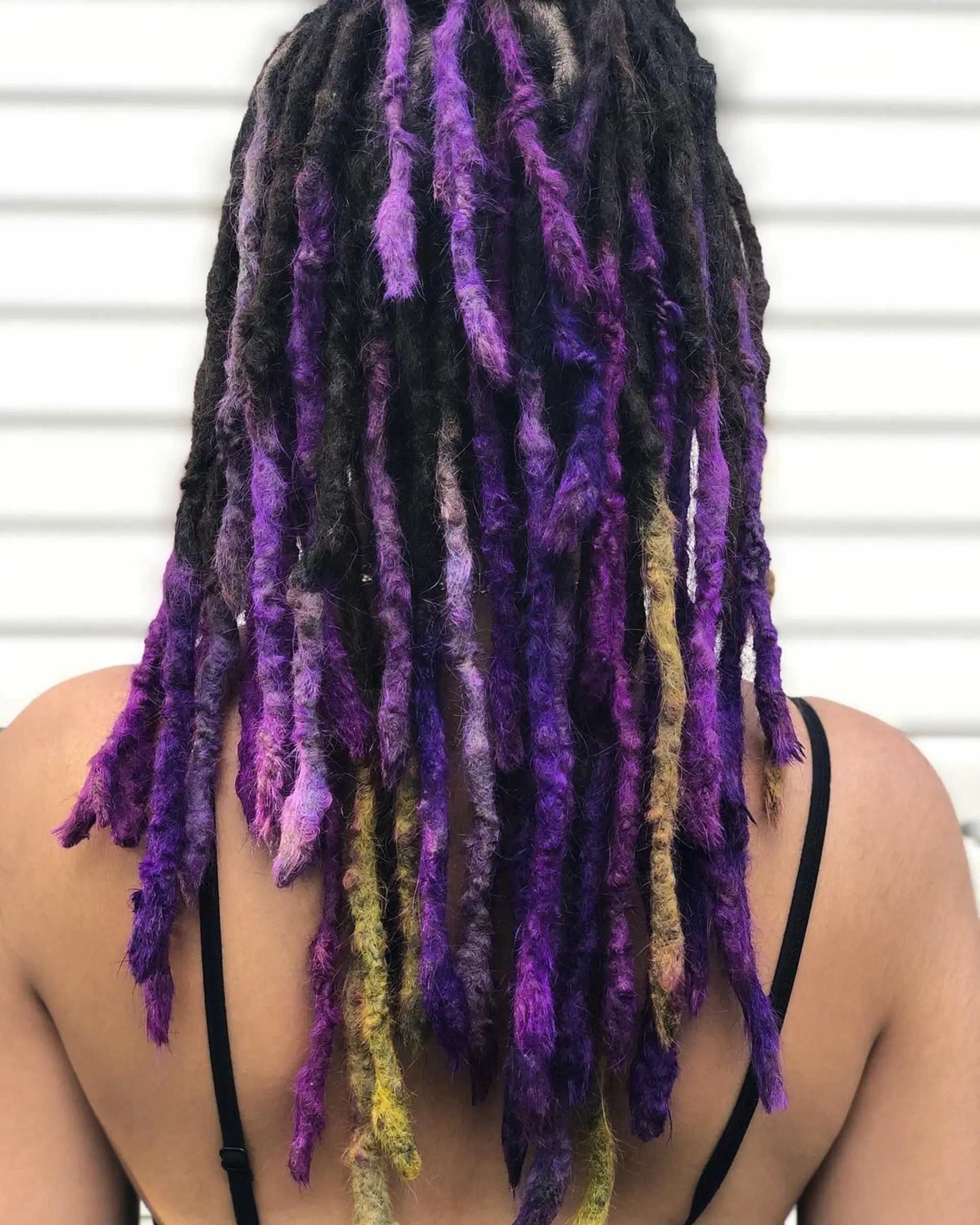 Vivid, medium-length dreadlocks with an electric purple and bright yellow ombre effect, starting from a curly texture. 2