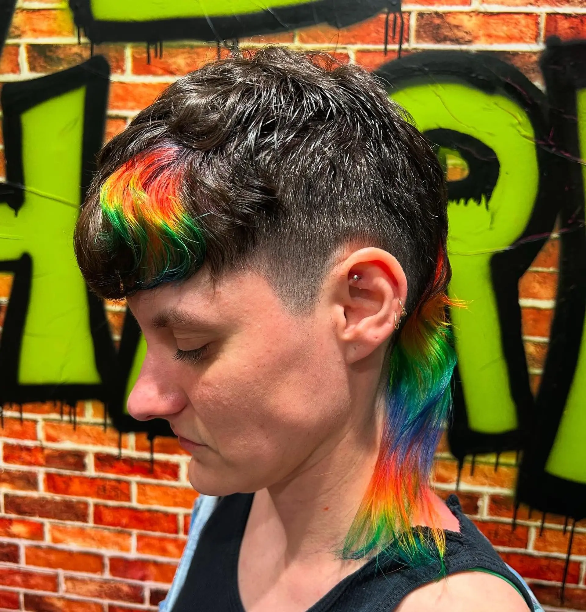 A modern edgy mullet featuring tapered faded sides, textured dark brown hair on top, and vibrant rainbow vivid accents placed in the blunt fringe and the elongated nape tail. 1