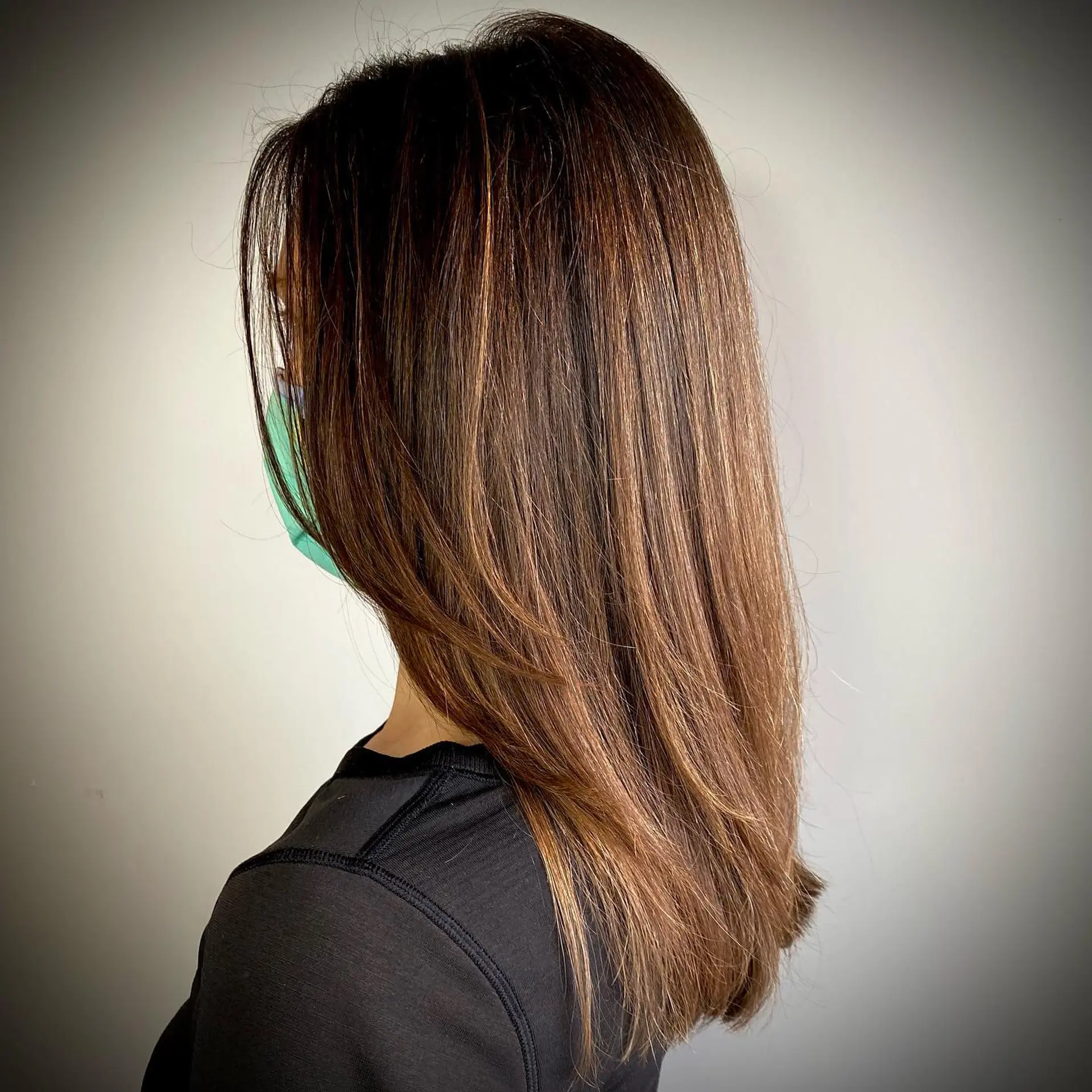 Straight, long dark brown hair styled smooth with fine, dimensional caramel babylights throughout. 1
