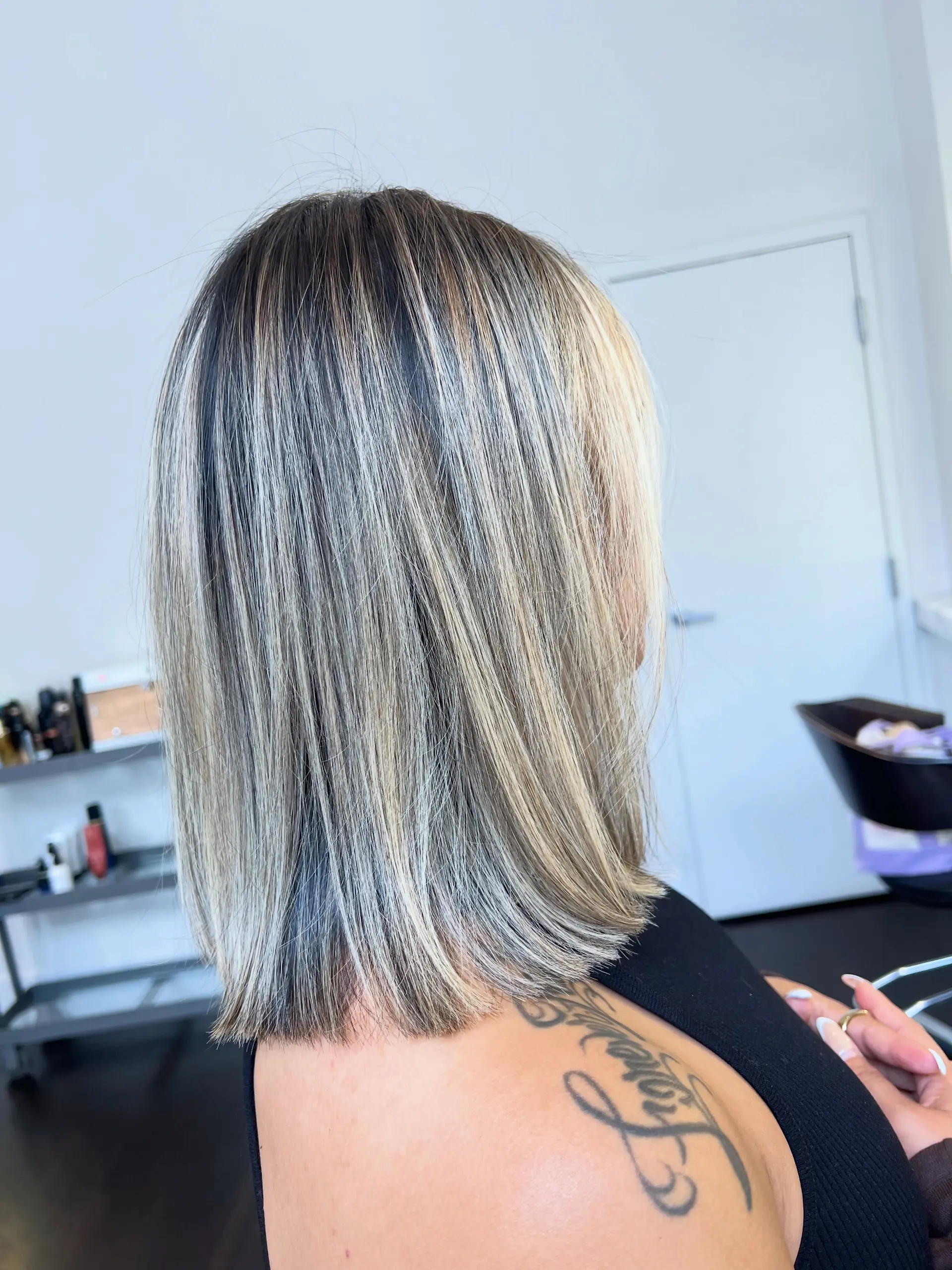 A sleek, one-length blunt lob falling at the collarbone with cool ash-blonde dimensional highlights over a dark base. 1