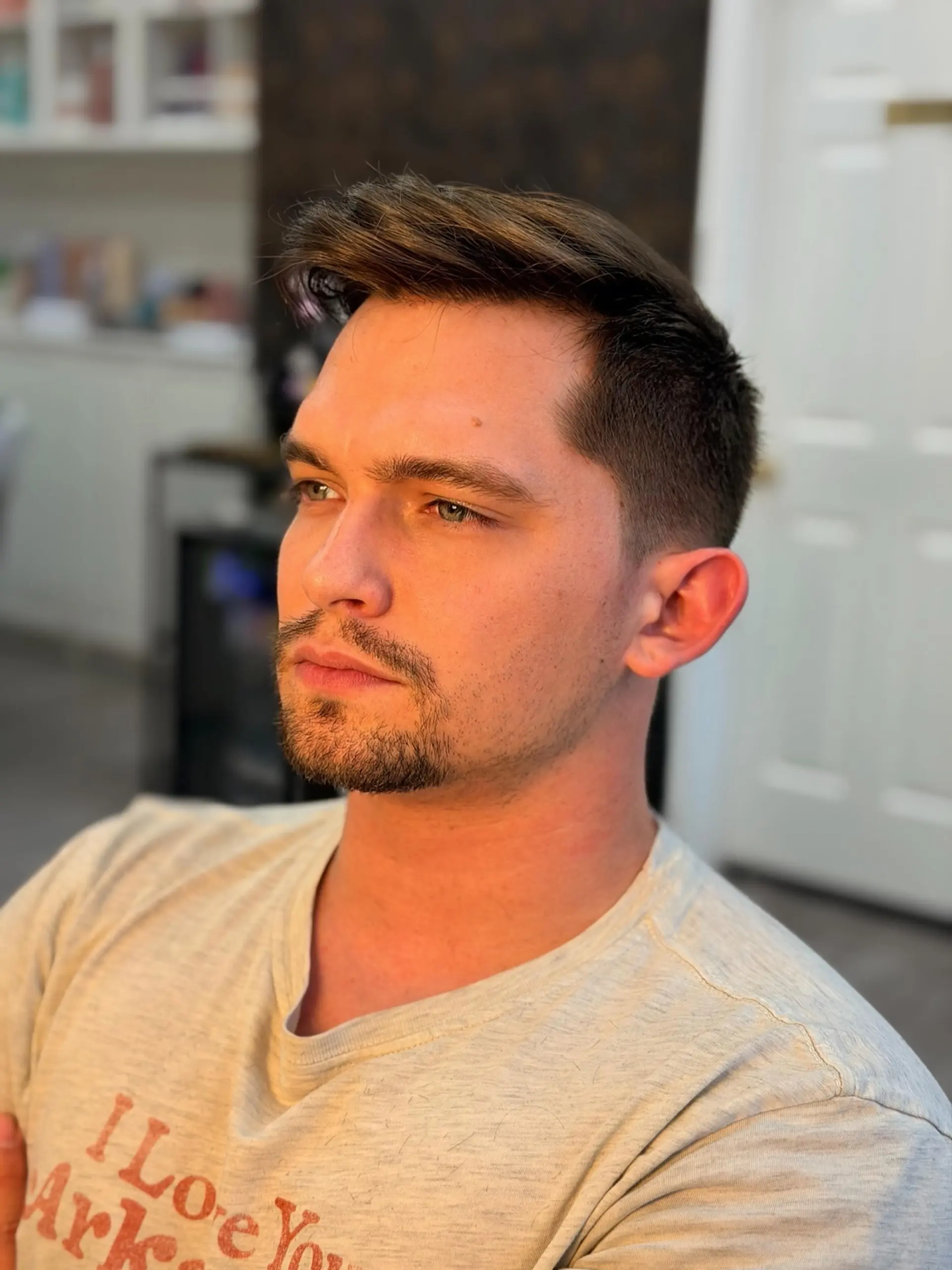 A clean men's haircut featuring a textured quiff brushed up and to the side, paired with neatly tapered sides and groomed facial hair. 1