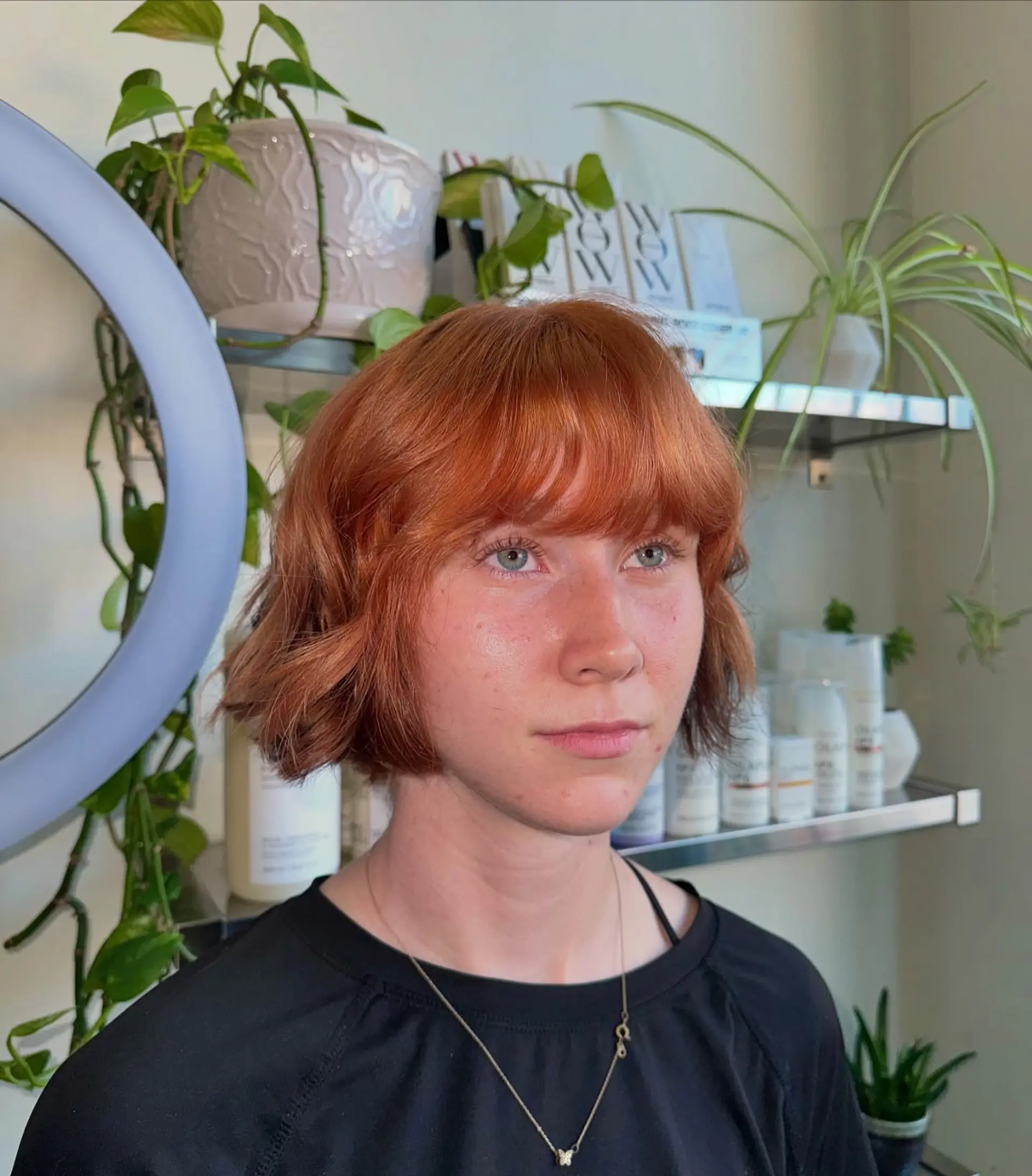 A textured jaw-length bob dyed in a vibrant copper tone, styled with soft waves and full front bangs. 1