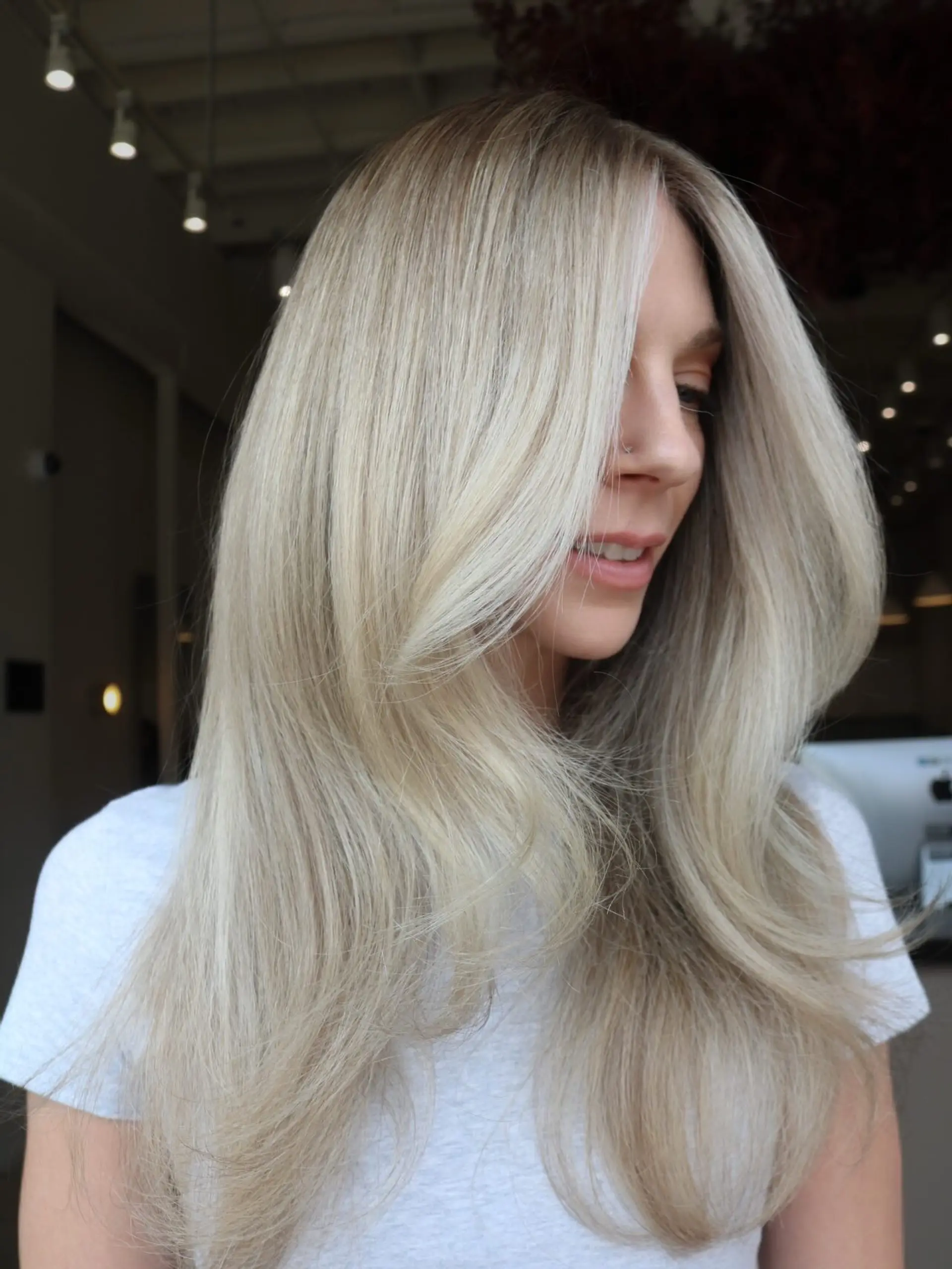 Long, bright neutral blonde hair featuring a rooted dimension, face-framing money piece, and a voluminous layered blowout. 1
