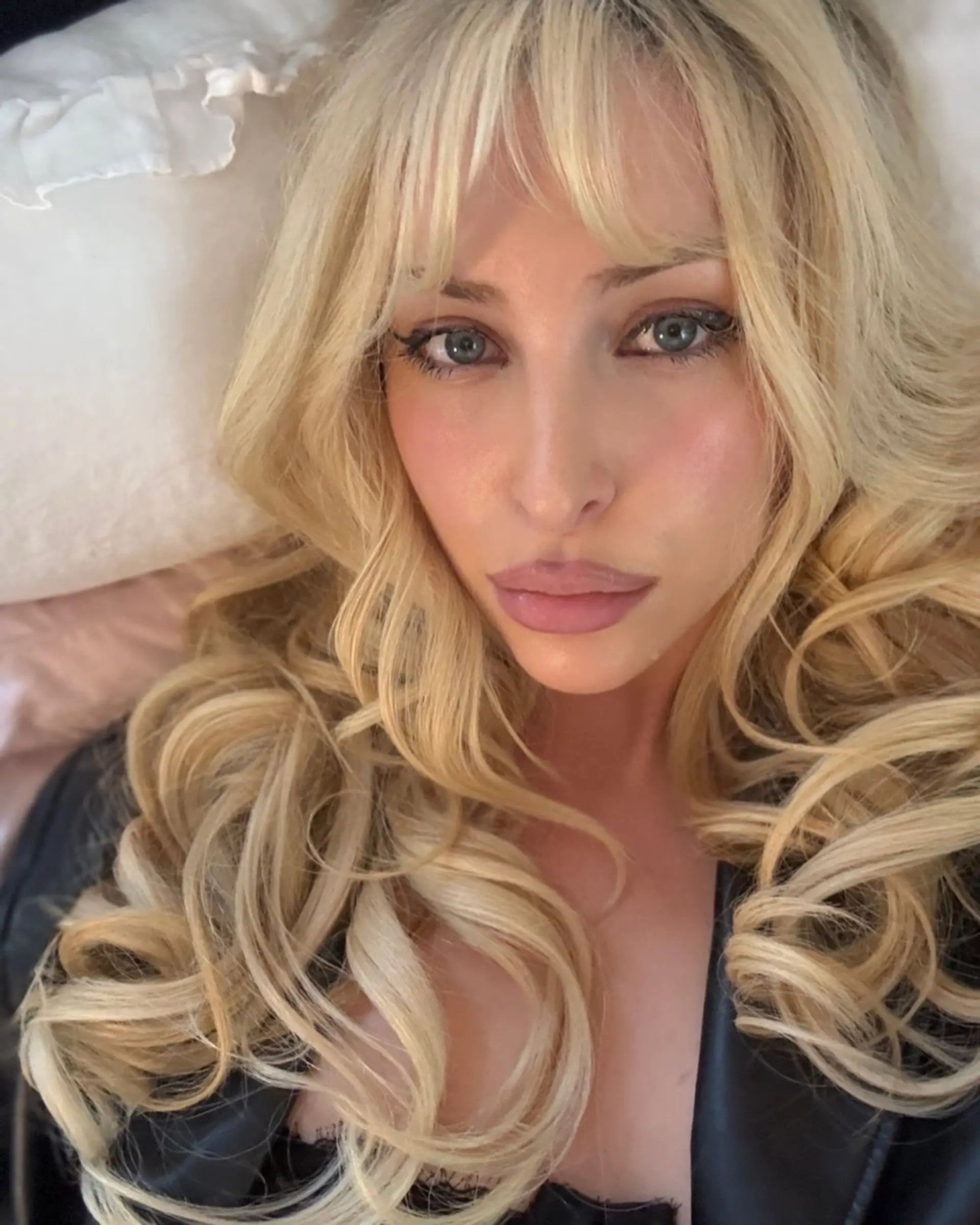 Long, voluminous platinum blonde hair styled with soft, defined curls and textured wispy bangs. 1