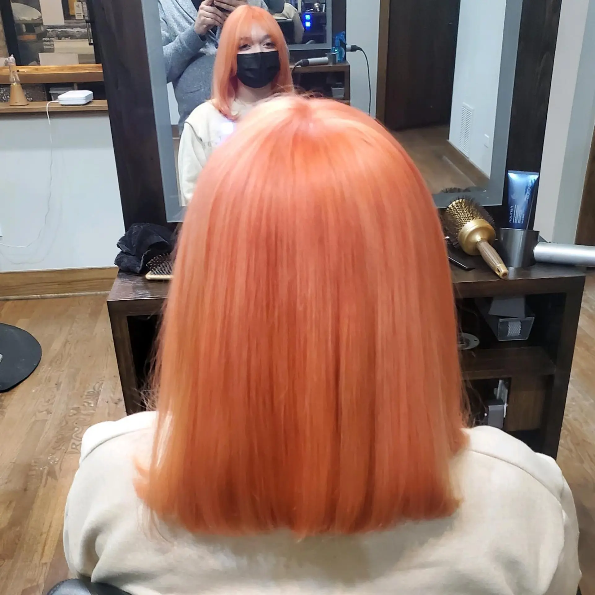 A blunt, shoulder-grazing medium lob dyed in an all-over pastel peach and vibrant orange tone, styled sleek and straight. 1