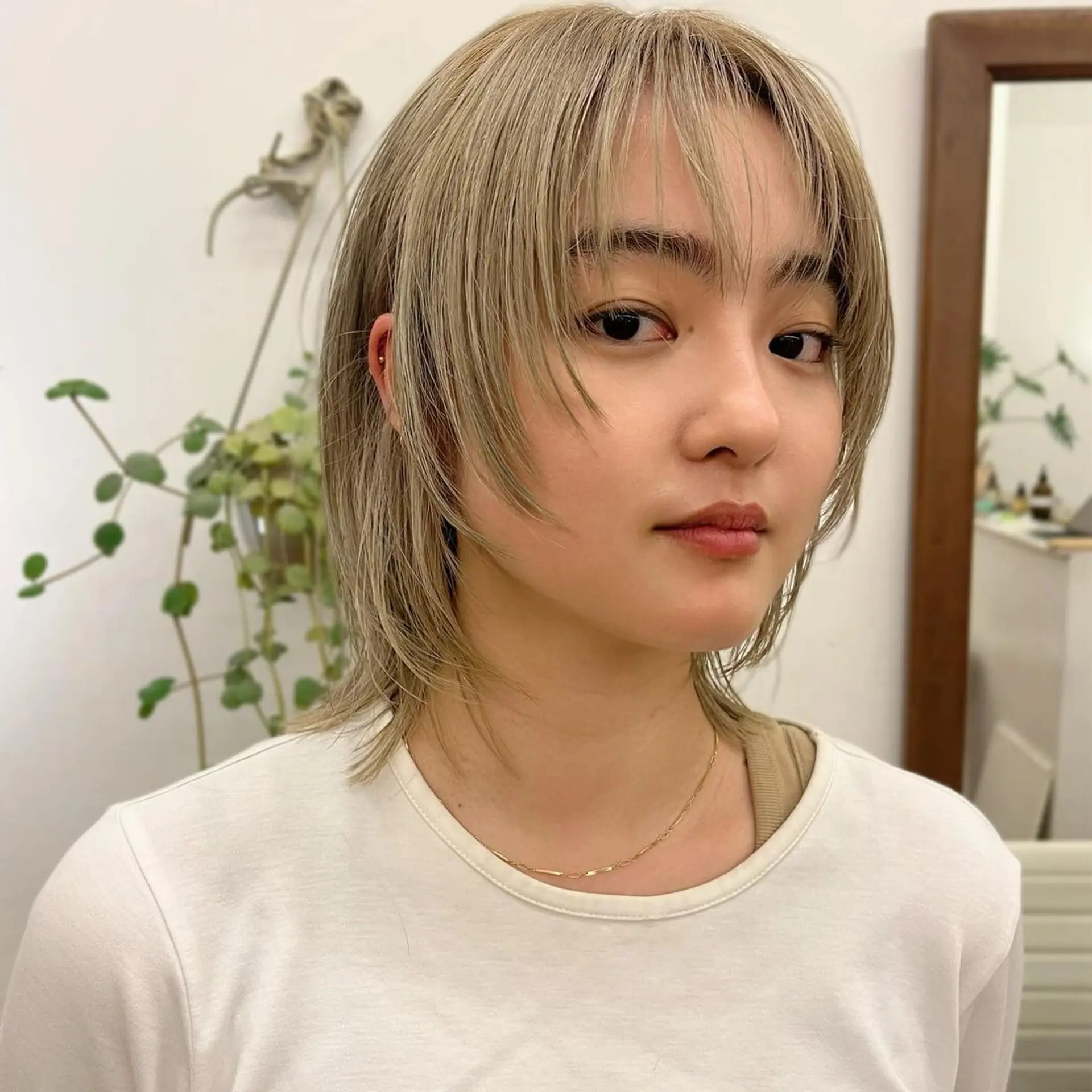 A short, straight blonde hairstyle with platinum highlights, featuring wispy bangs and feathered layers for a textured and dynamic appearance. 2