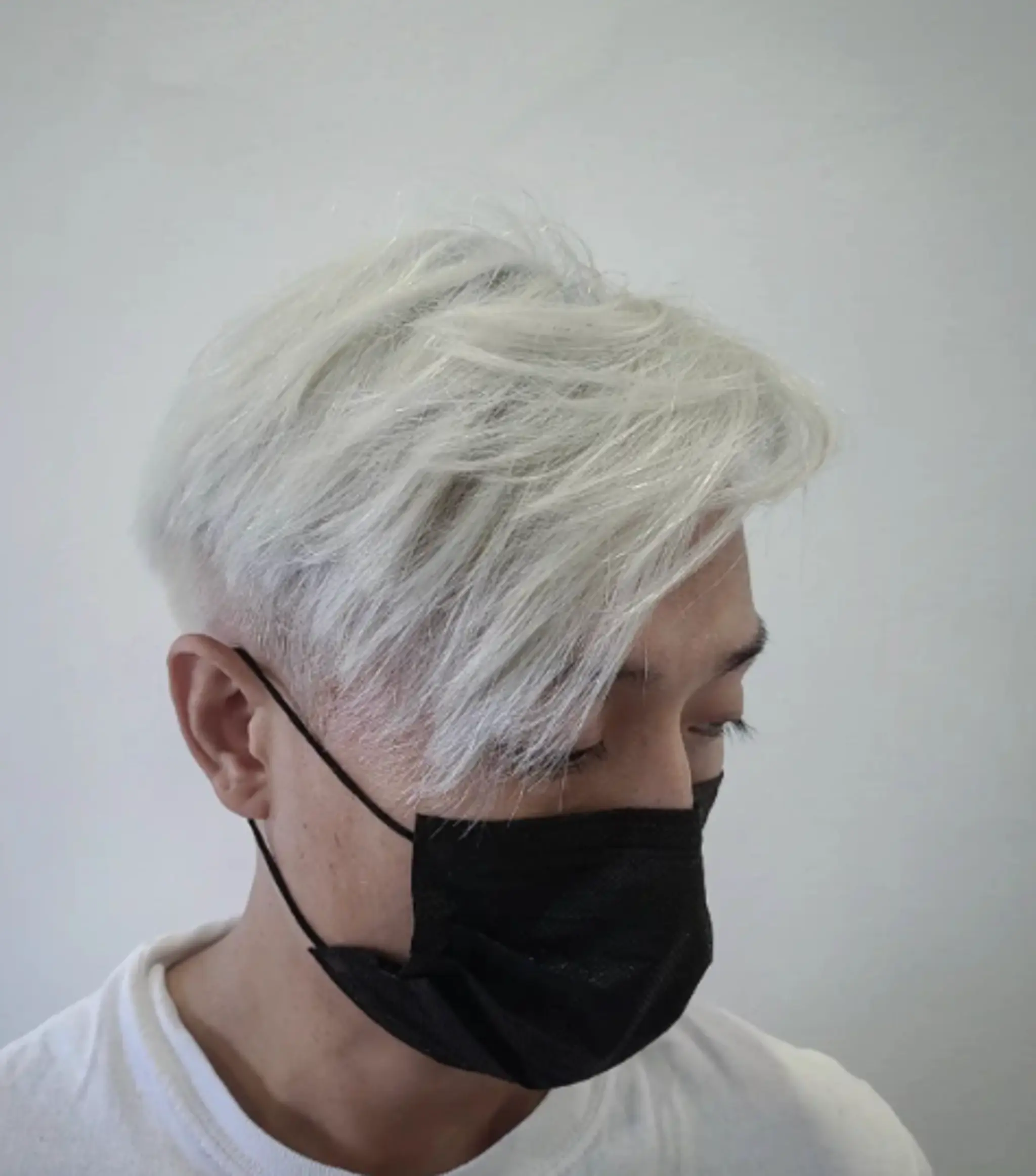 Platinum blonde straight hair with an undercut and textured top, featuring soft layers and an asymmetrical fringe that sweeps to the side.