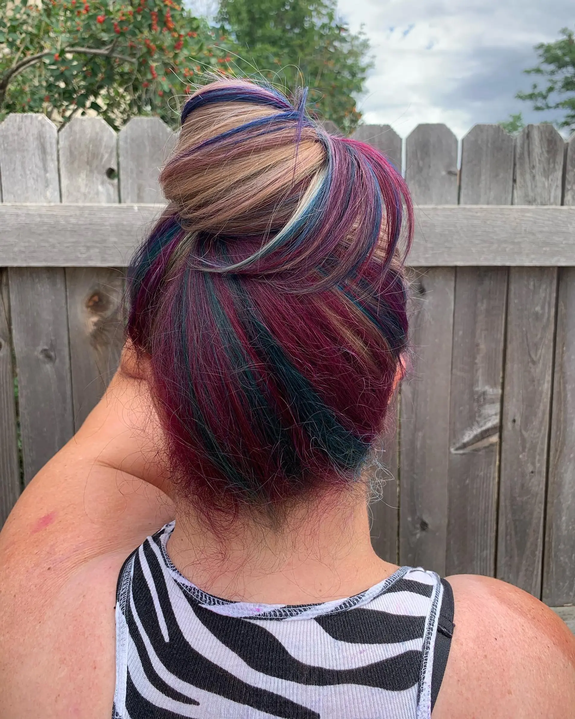 A top knot bun showcasing multicolor vivid highlights woven throughout blonde hair. 1