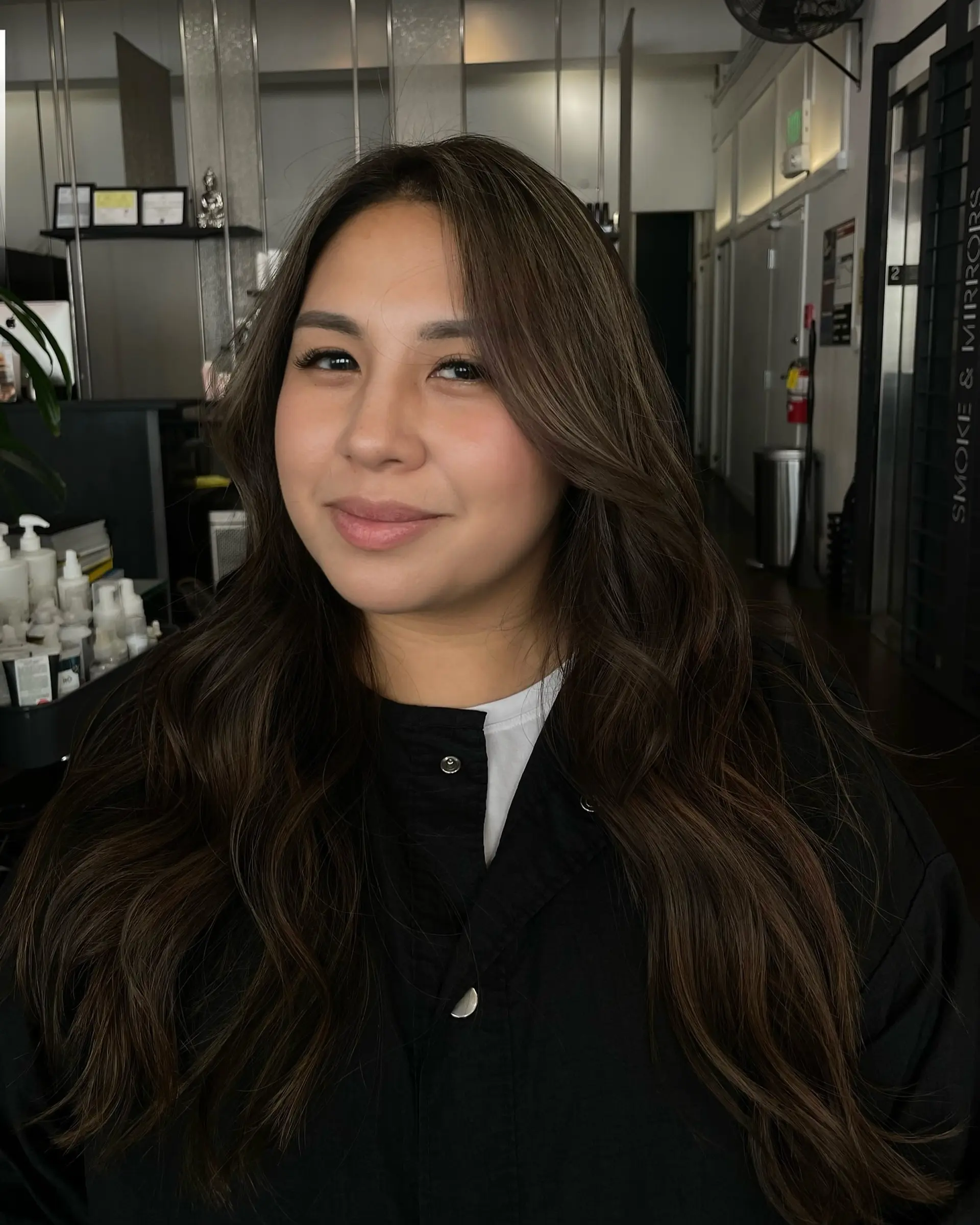 Long brunette hair styled in loose waves with seamless, dimensional highlights and face-framing layers. 1