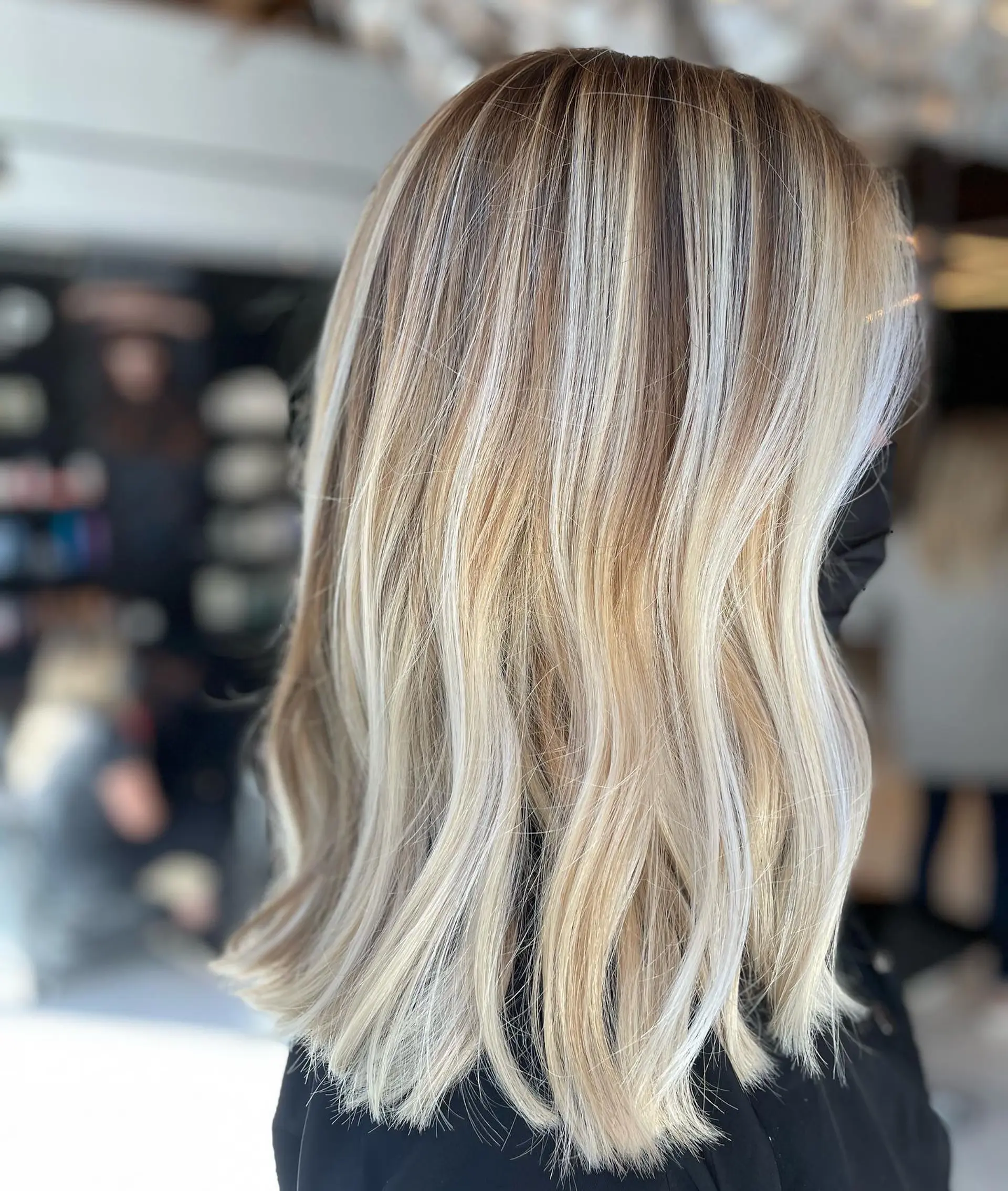 Collarbone-length lob styled with loose, relaxed waves highlighting a multi-tonal blonde balayage over a natural light brown base. 1