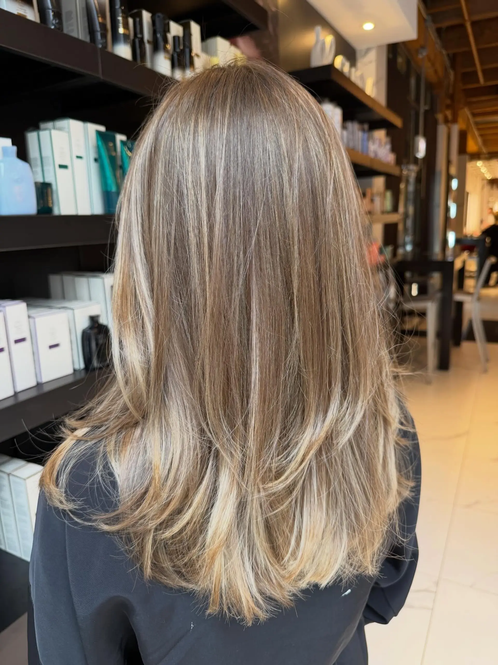 Long hair featuring soft blonde balayage ribbons blended over a light brown base, styled with feathered layers. 1