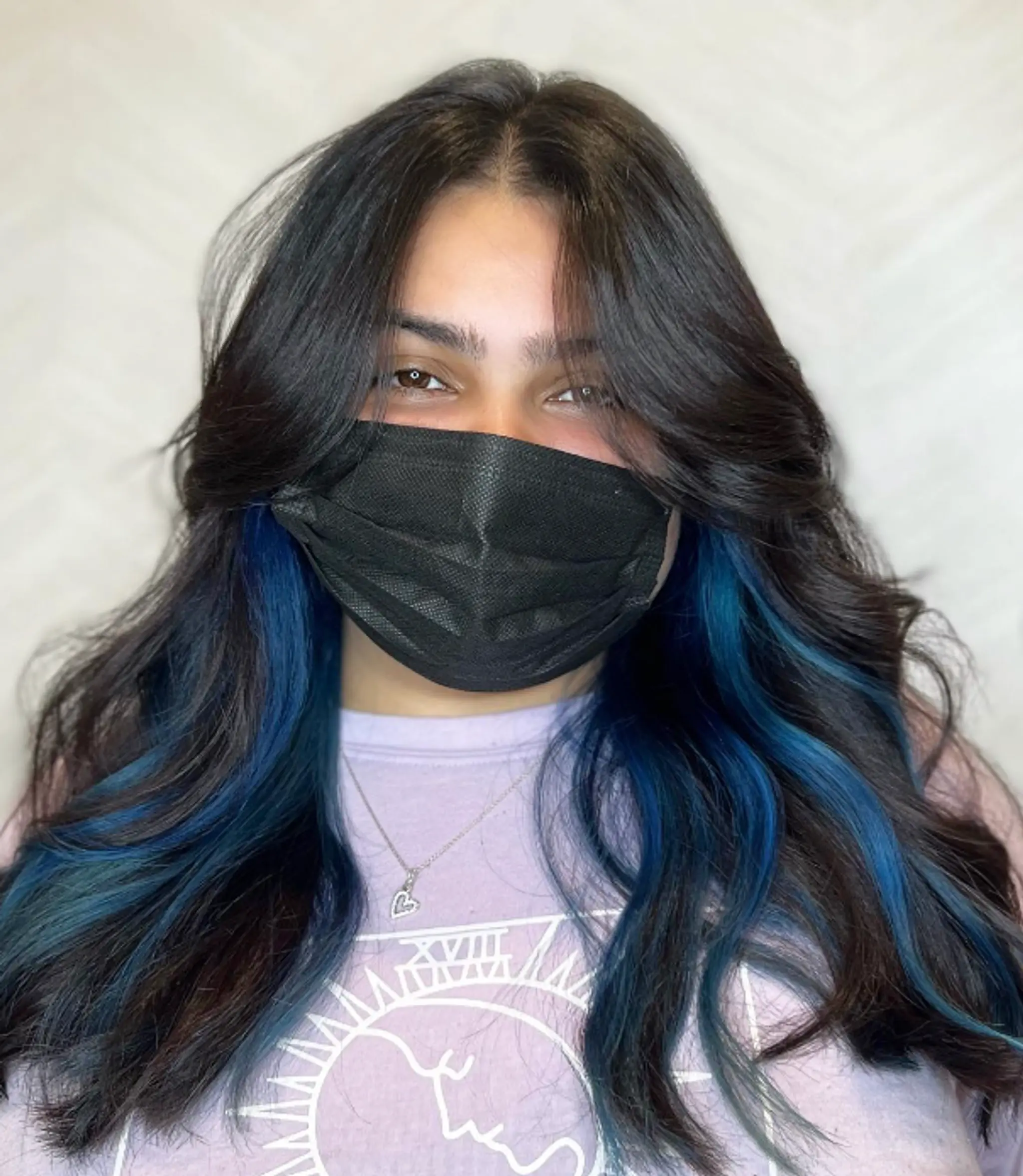 Long, flowing black hair with striking blue streaks. Wavy texture with face-framing layers and soft curls for a vibrant and trendy look.