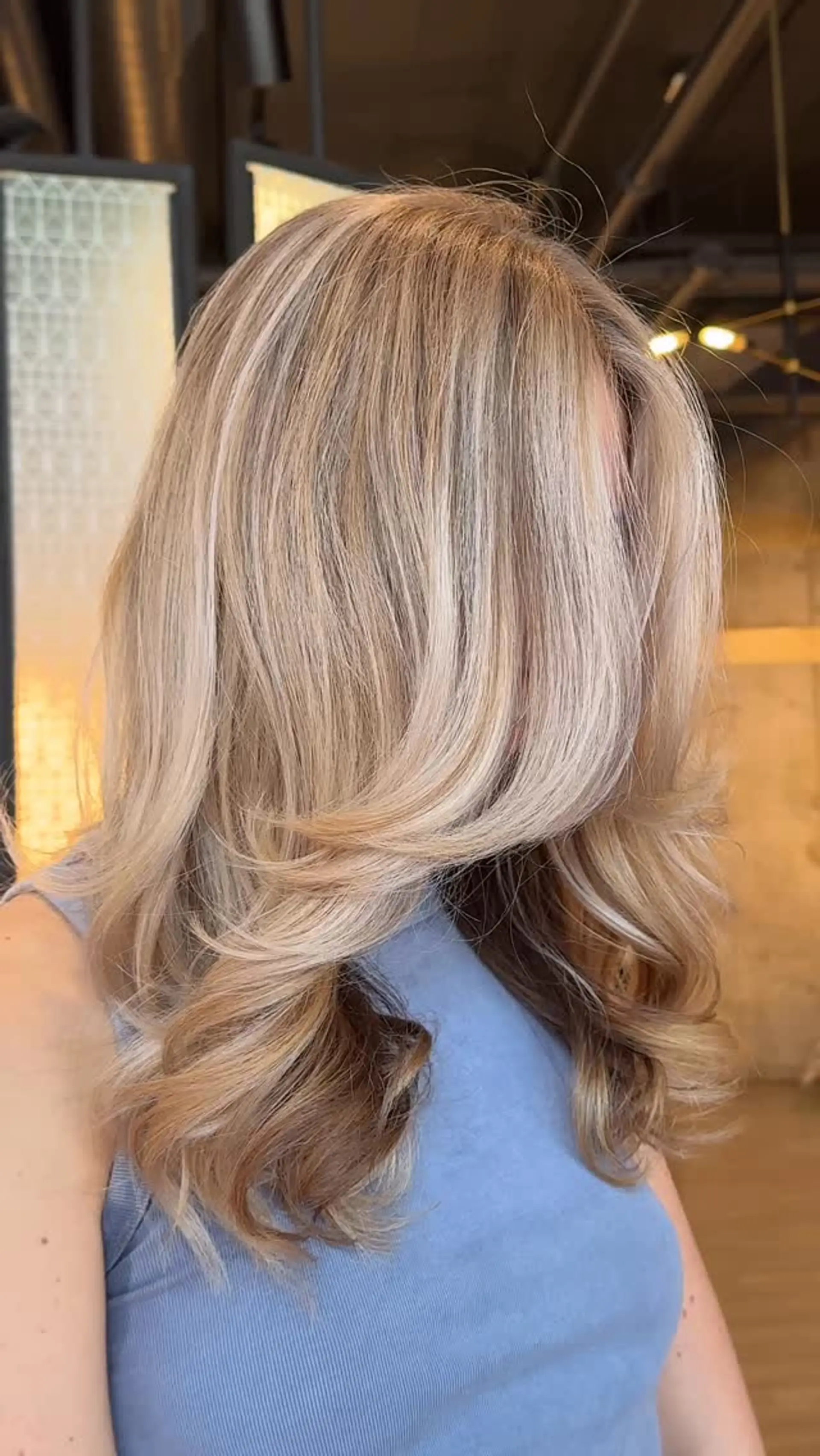 Medium-length dimensional blonde hair cut with curtain, face-framing layers and styled in a bouncy blowout. 1