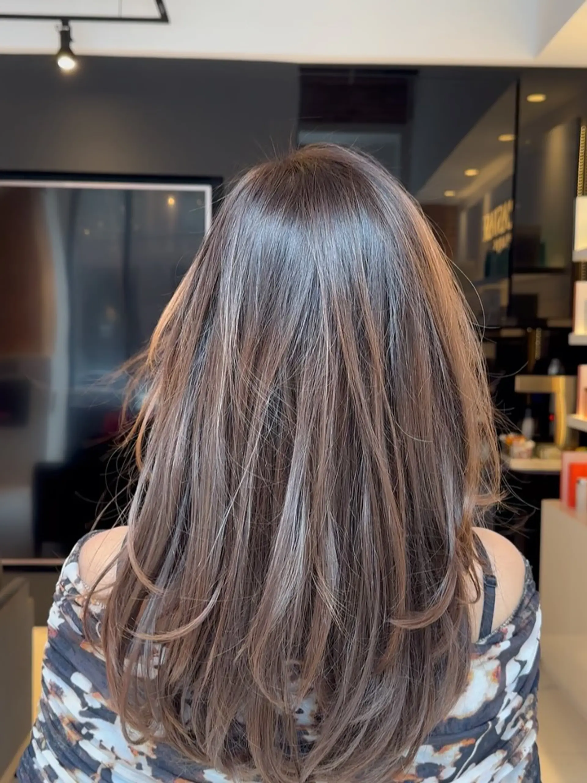 Long, layered brunette hair featuring soft balayage highlights and a smooth, glossy blowout with gentle inward curls at the ends. 1