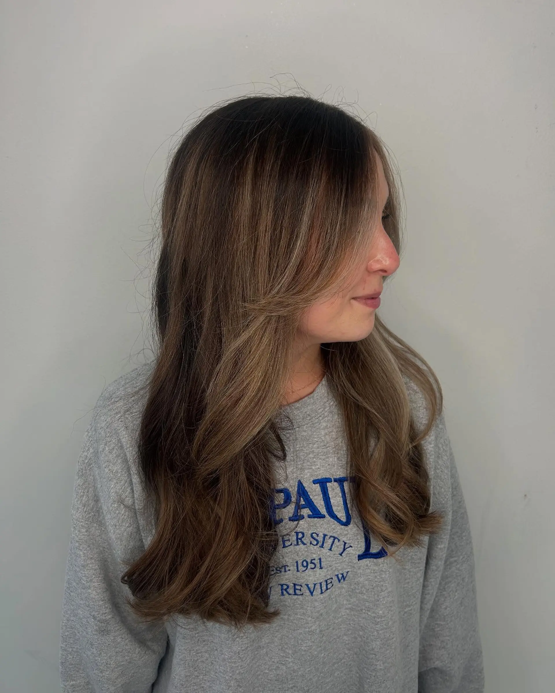 Long dark brown hair featuring a blended balayage with soft ash brown highlights and face-framing layers styled into gentle waves. 1