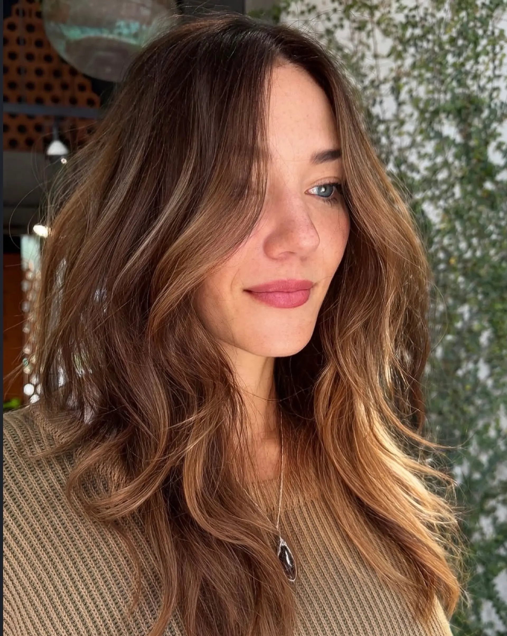 Long dimensional brunette hair styled in loose, textured waves with face-framing layers. 1