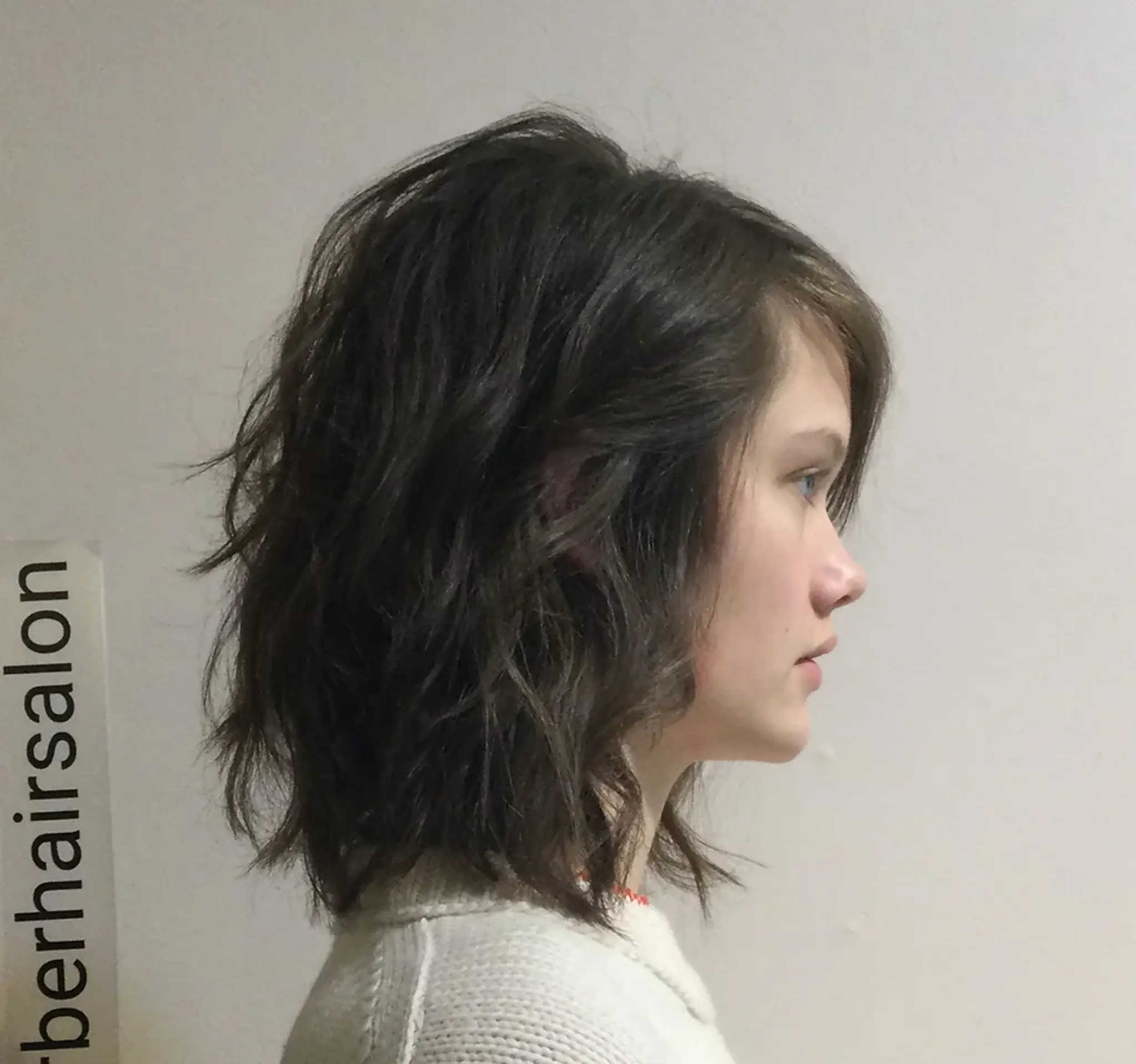 The hairstyle is a medium-length, dark brown wavy look with textured layers and voluminous roots, giving it a tousled, casual appeal.
