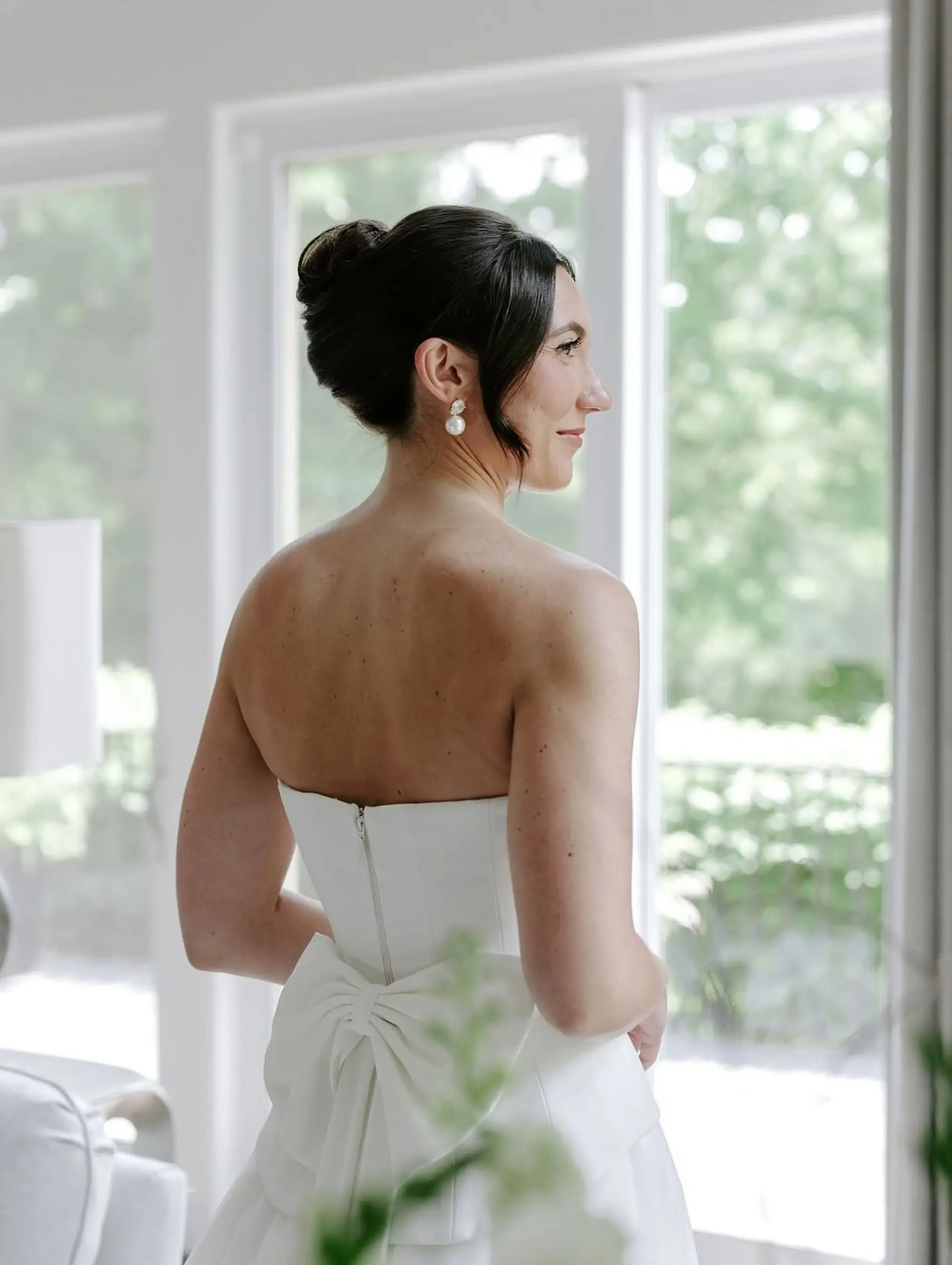 An elegant, sleek bridal updo featuring a polished high-to-mid bun with delicate face-framing pieces. 1