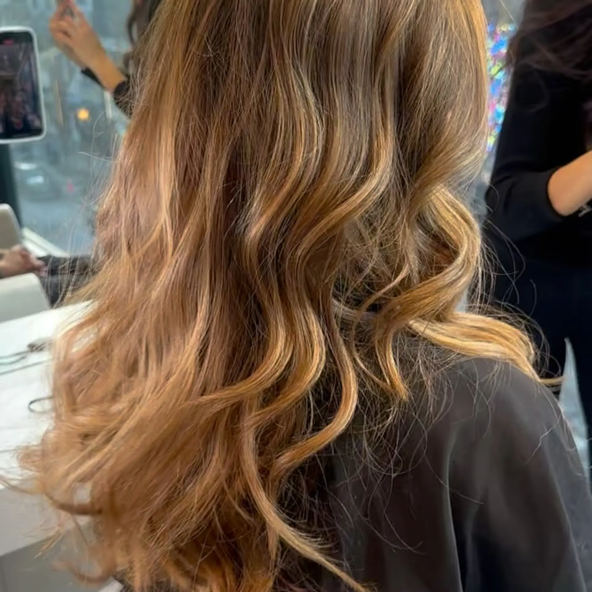 Long hair featuring warm bronde balayage tones styled in loose, dimensional waves. 1