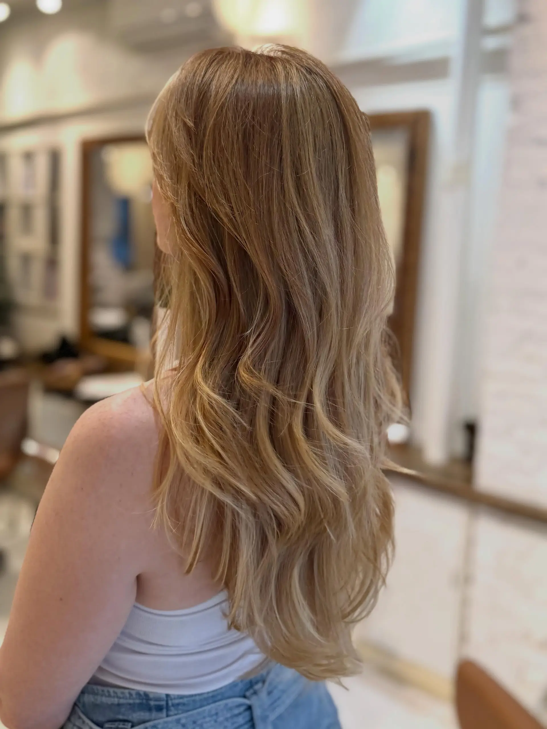 Long cascading hair featuring a soft, seamless airtouch blonde balayage styled into gentle loose waves. 1