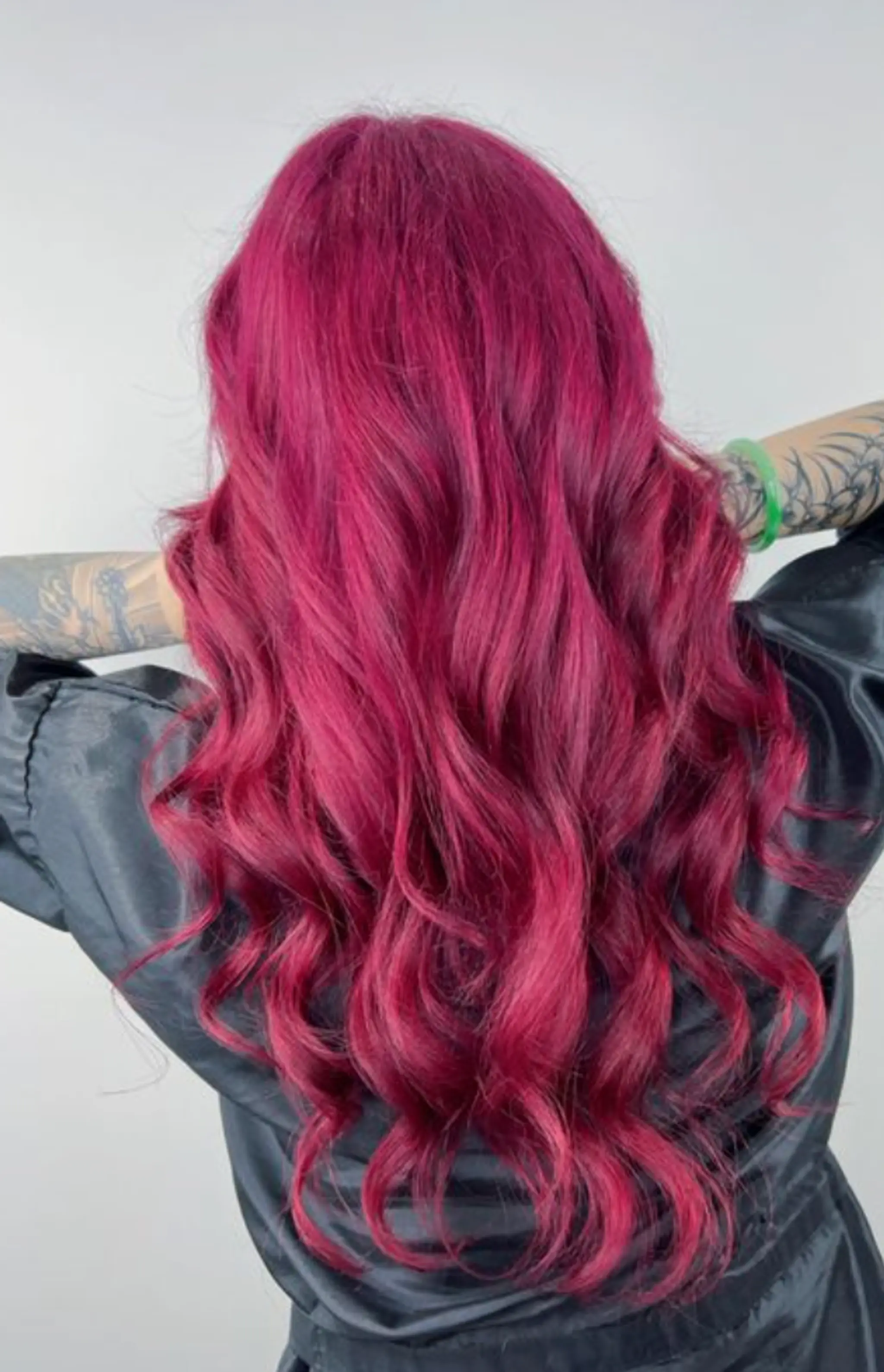 The hairstyle features vibrant magenta waves cascading down to a long length, characterized by face-framing layers that enhance the wavy texture. 2