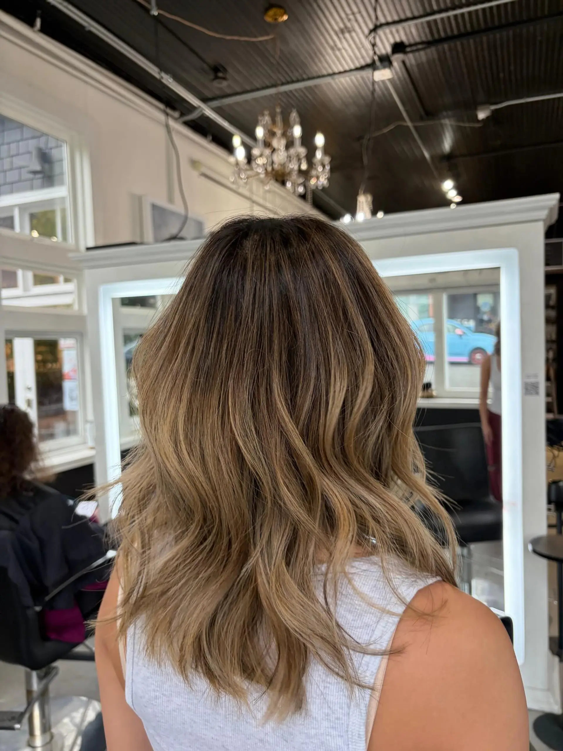Medium-length dimensional color with soft, beachy waves blending warm caramel highlights over a natural brown base. 1