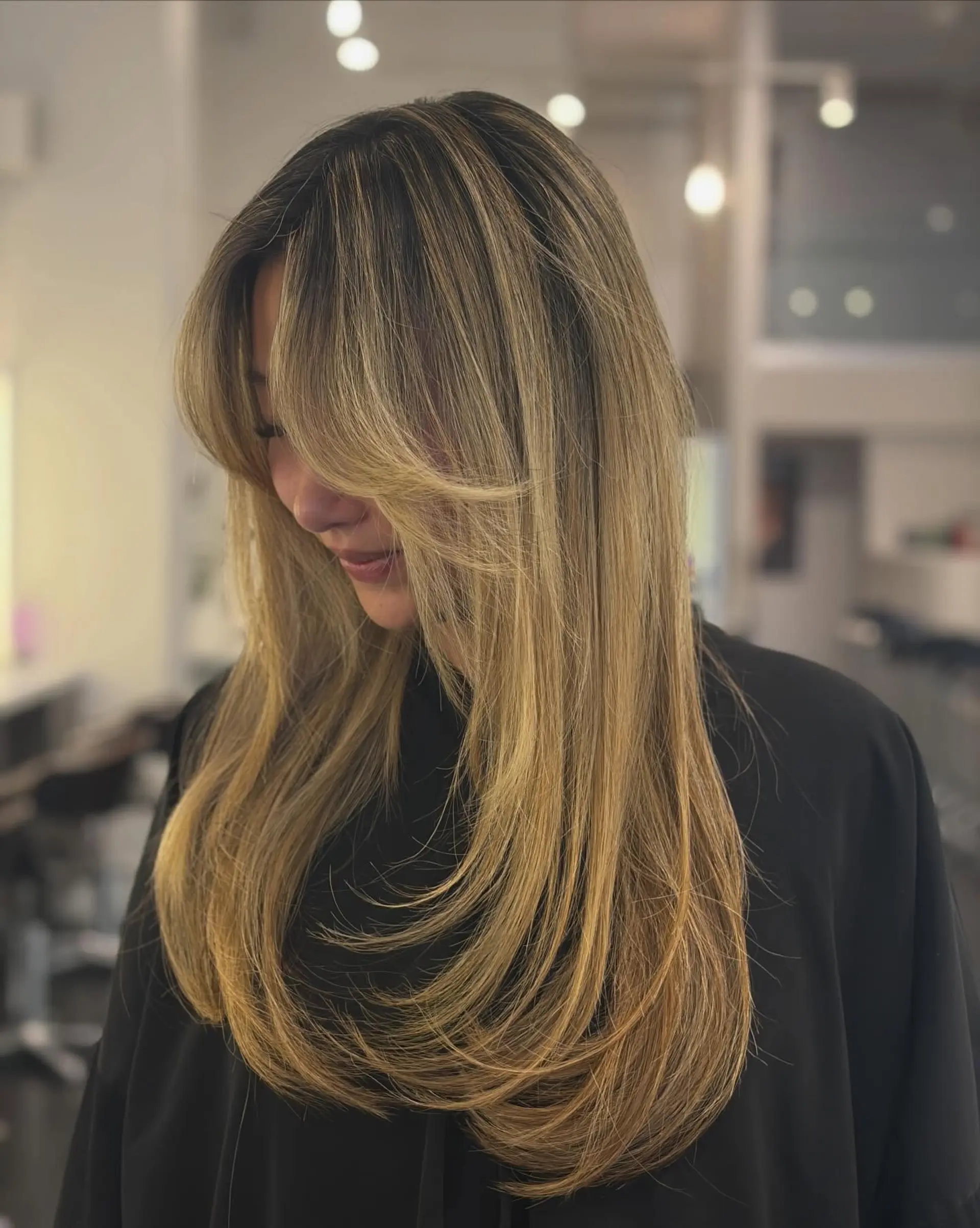 Long layered hair featuring soft curtain bangs and a smooth, round-brushed blowout with tapered ends curving gracefully inward. 1