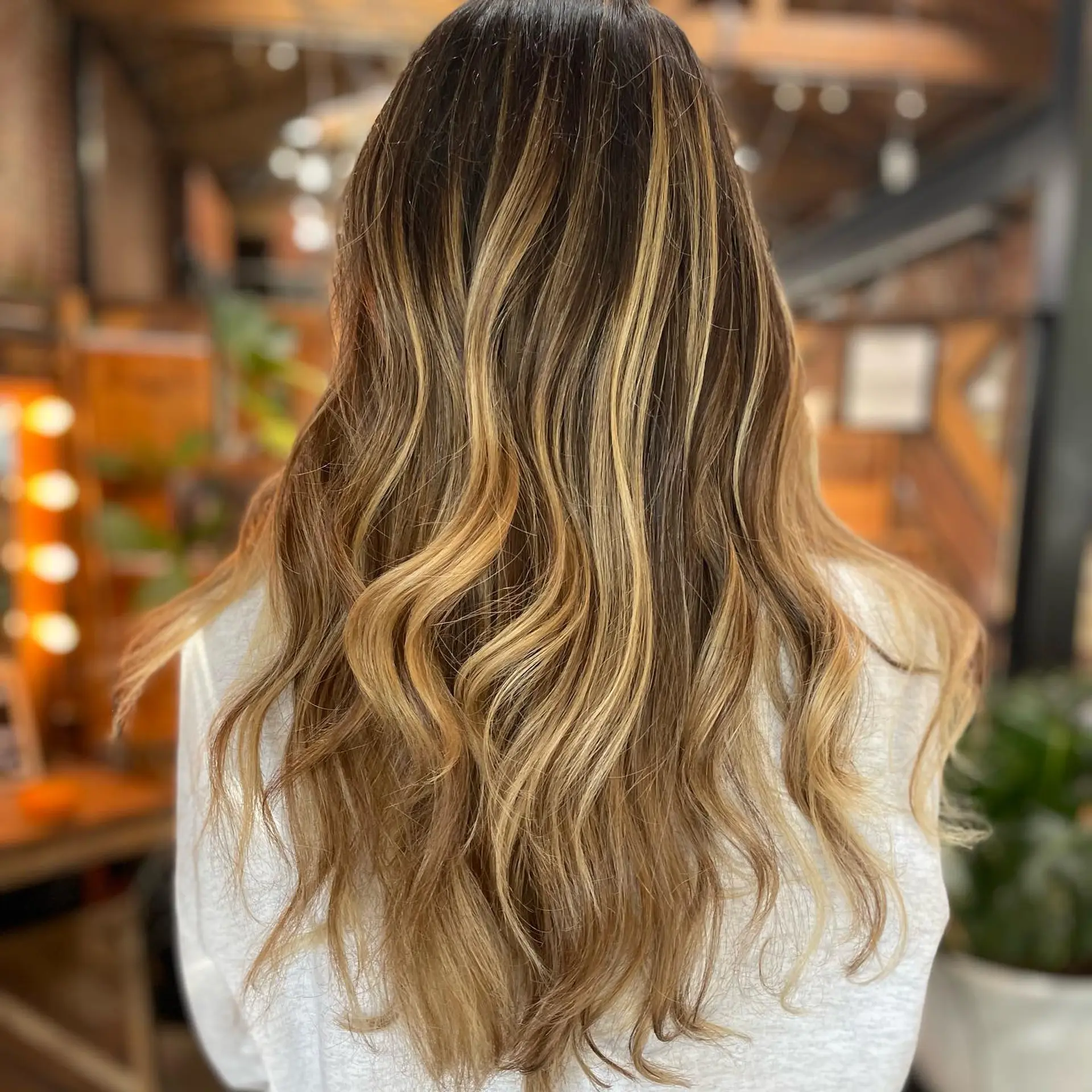 Long dimensional dark brown hair highlighted with warm honey-caramel balayage and styled in soft loose waves. 1