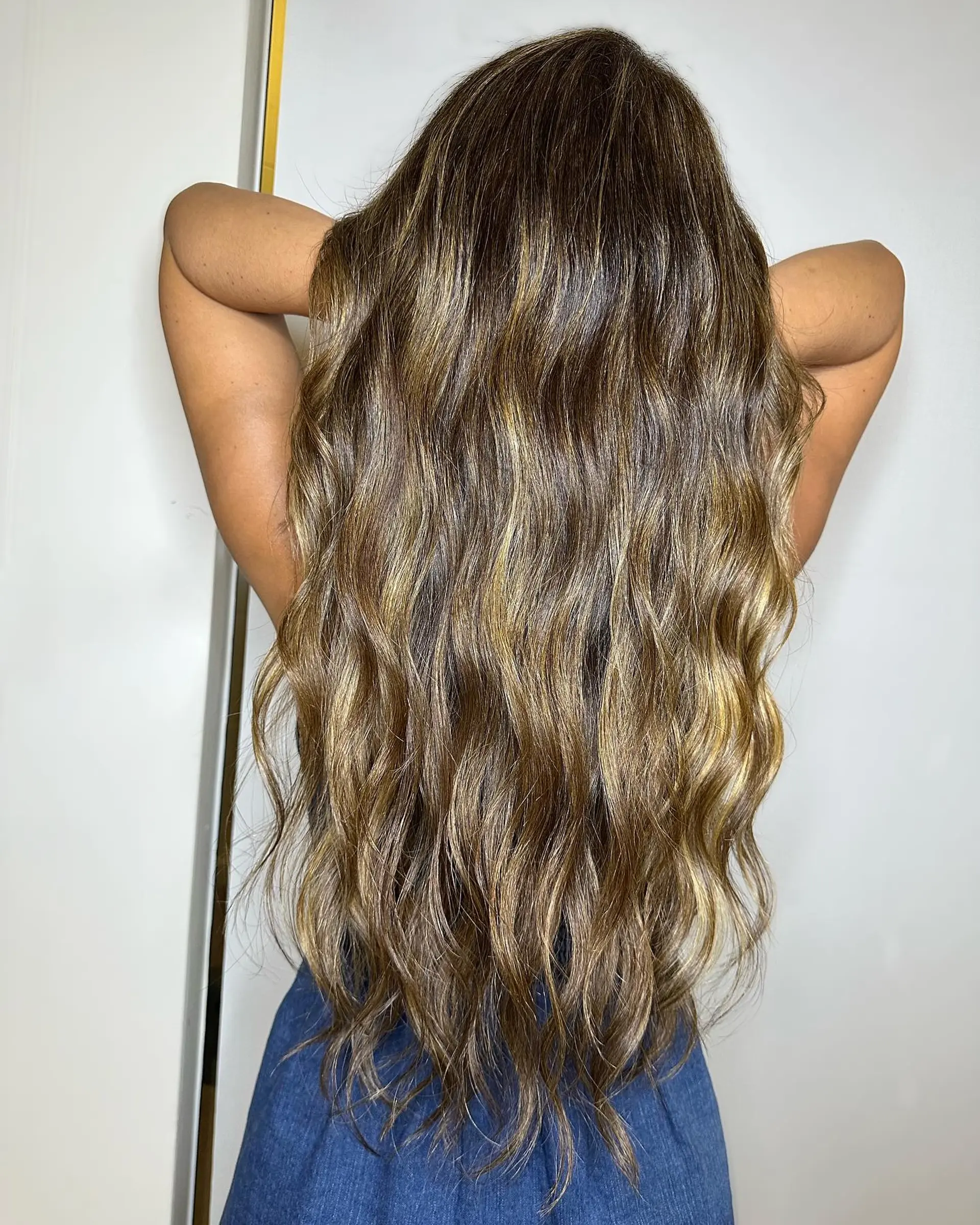 Extra-long brunette hair styled with dimensional golden babylights, long layers, and soft blowout waves. 1