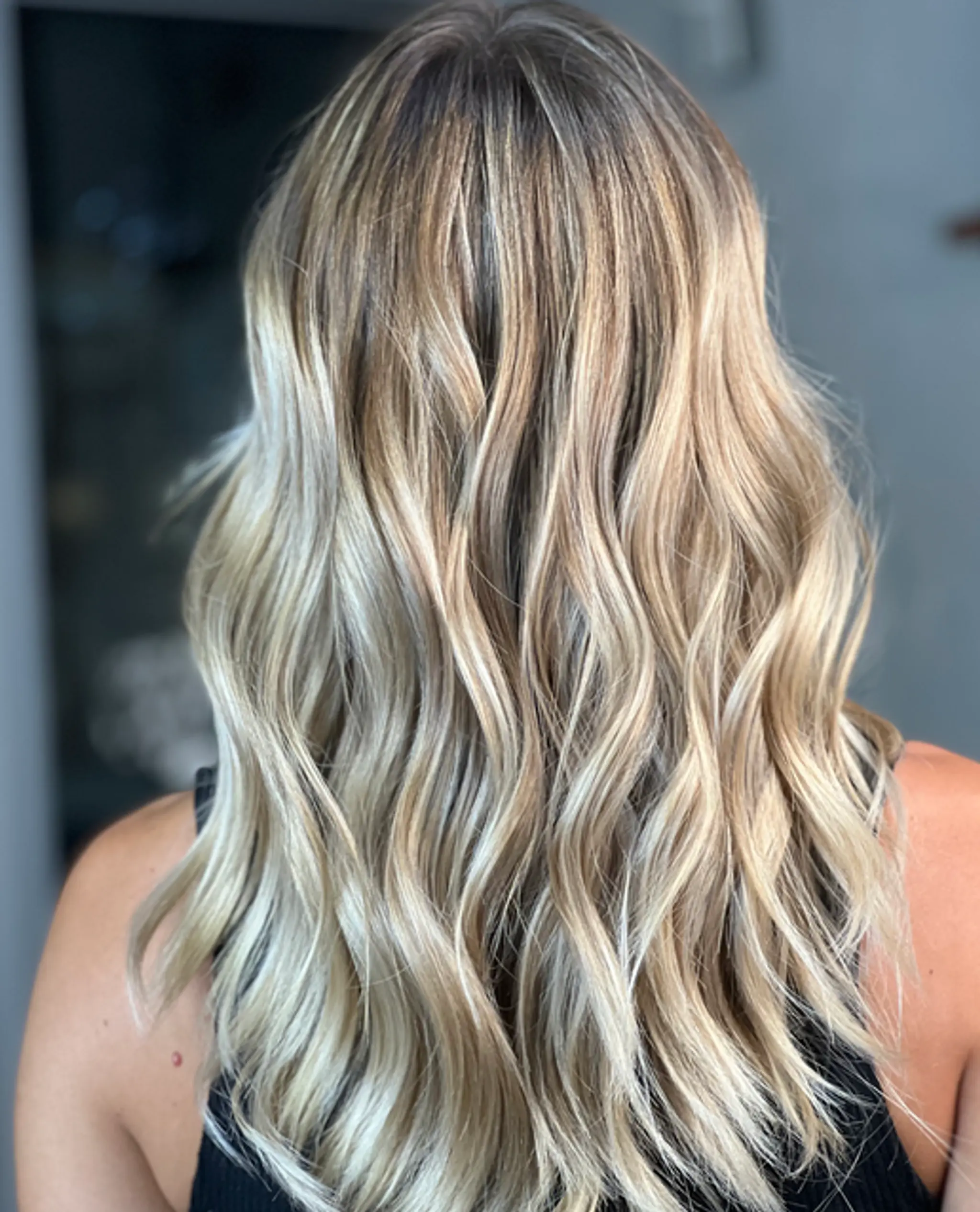 A long, wavy hairstyle with blonde, honey, and golden hues, featuring balayage and natural roots for a voluminous and sun-kissed look.