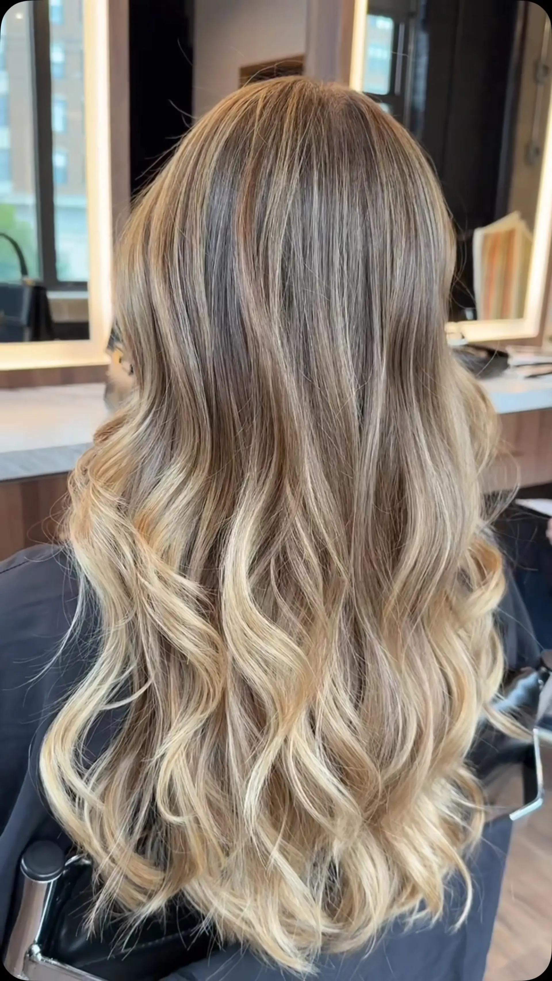 Long layered hair enhanced with dimensional honey blonde highlights and styled in soft loose waves. 1