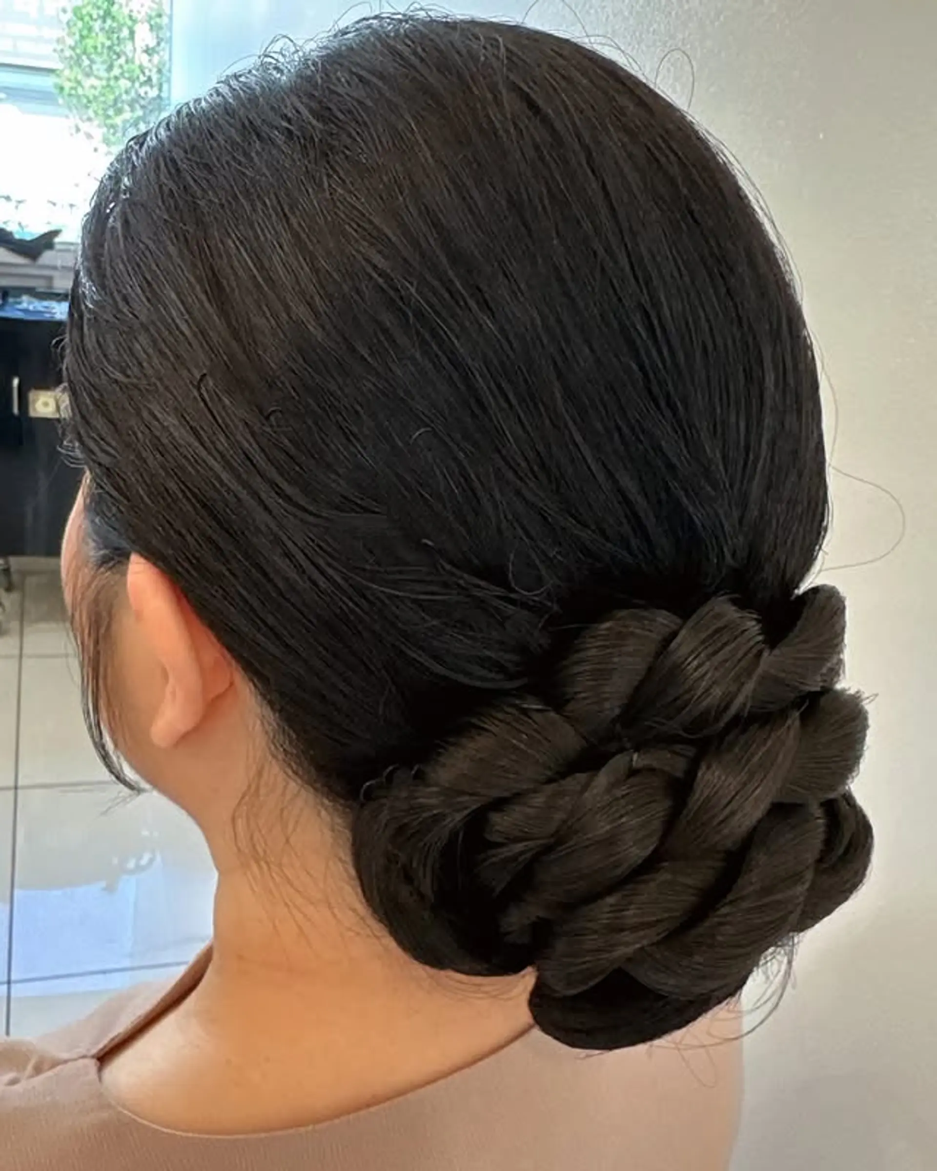 This style features the hair neatly gathered into a braided bun at the back of the head. 1