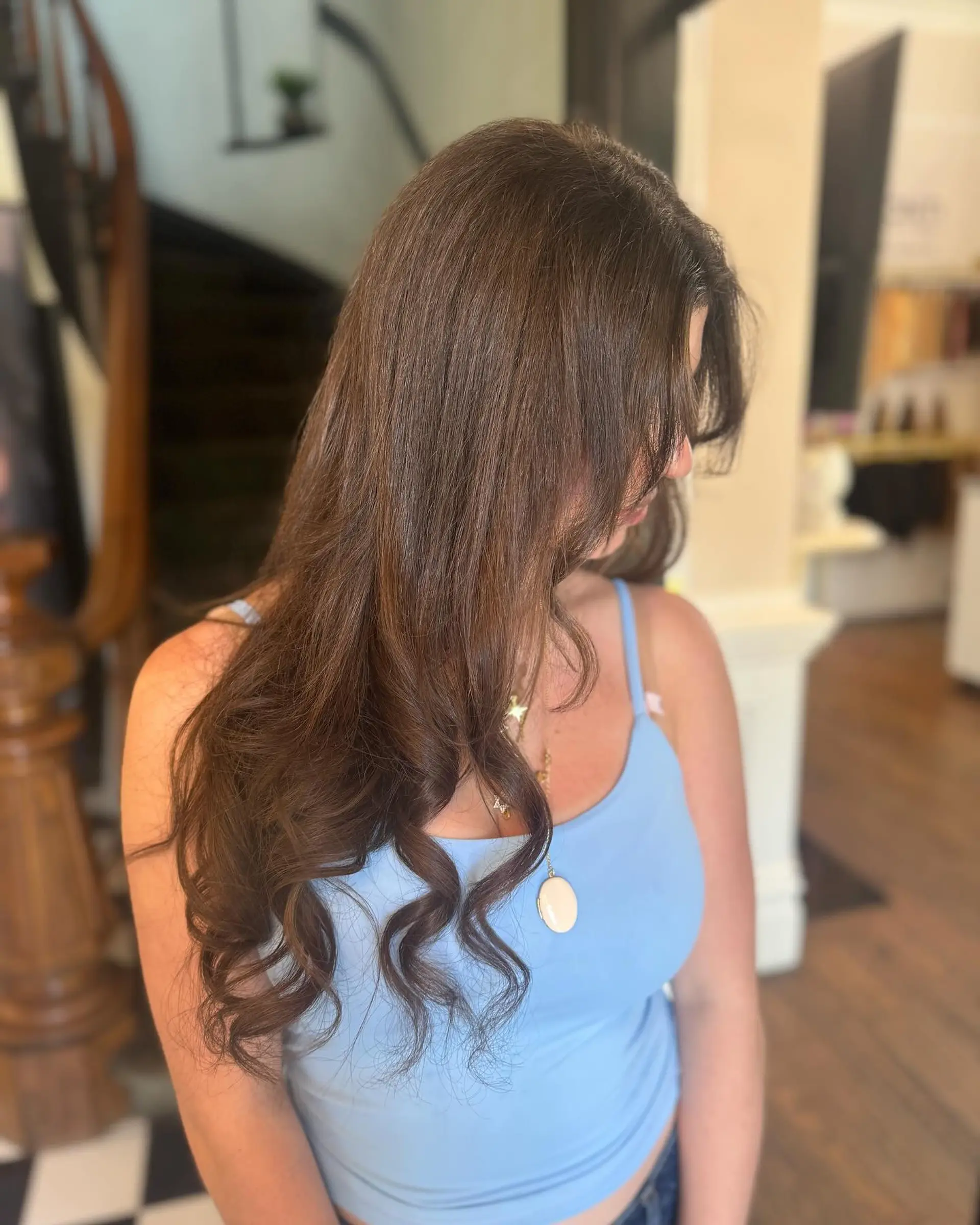 Long brunette hair styled into a silky smooth blowout featuring defined, bouncy curls toward the ends. 1