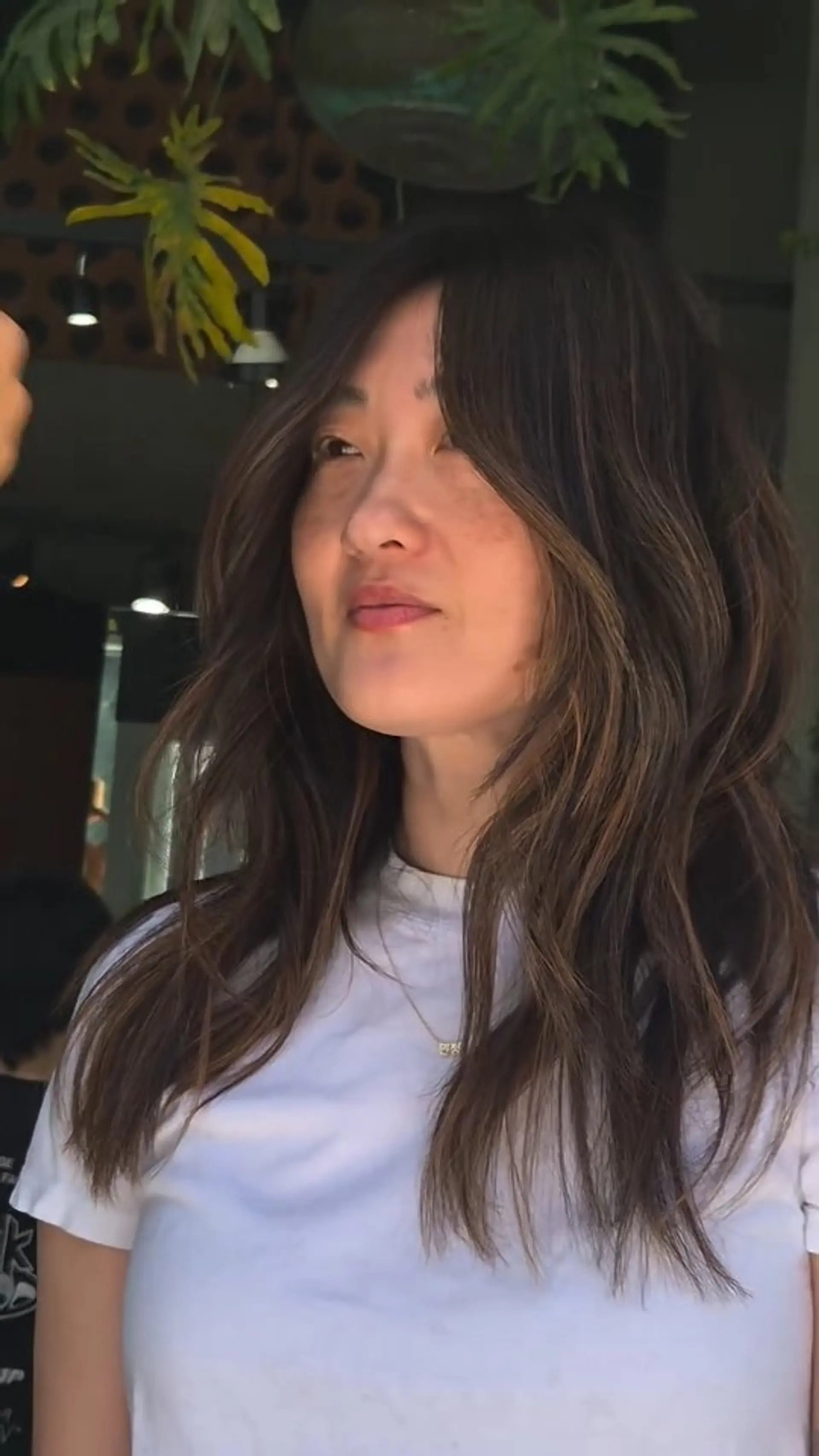 Layered brunette haircut with soft curtain bangs and subtle balayage highlights styled in loose, textured waves. 1