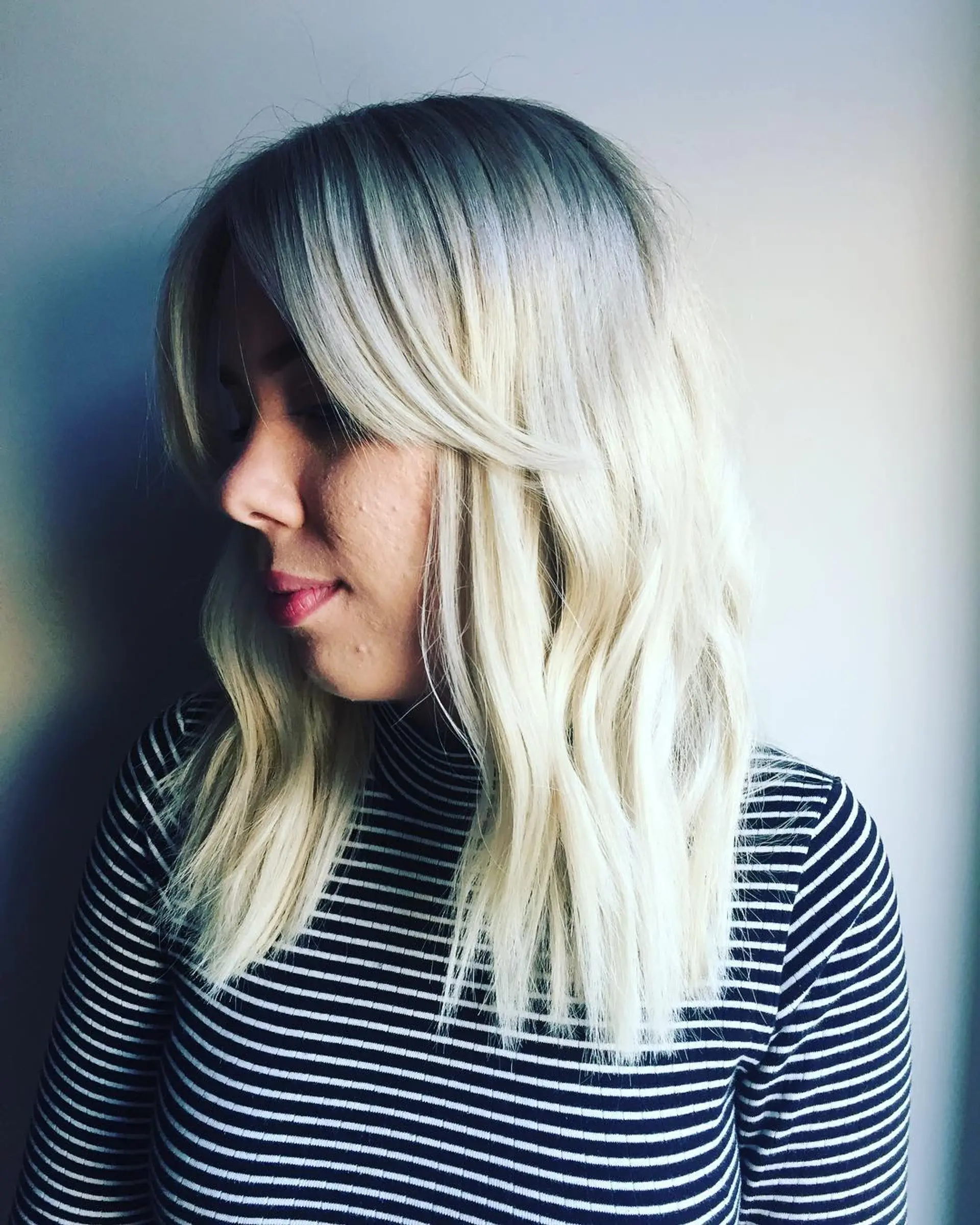 Wavy medium-length hair with a modern platinum blonde color and contrasting dark shadow root, complete with soft side bangs. 1