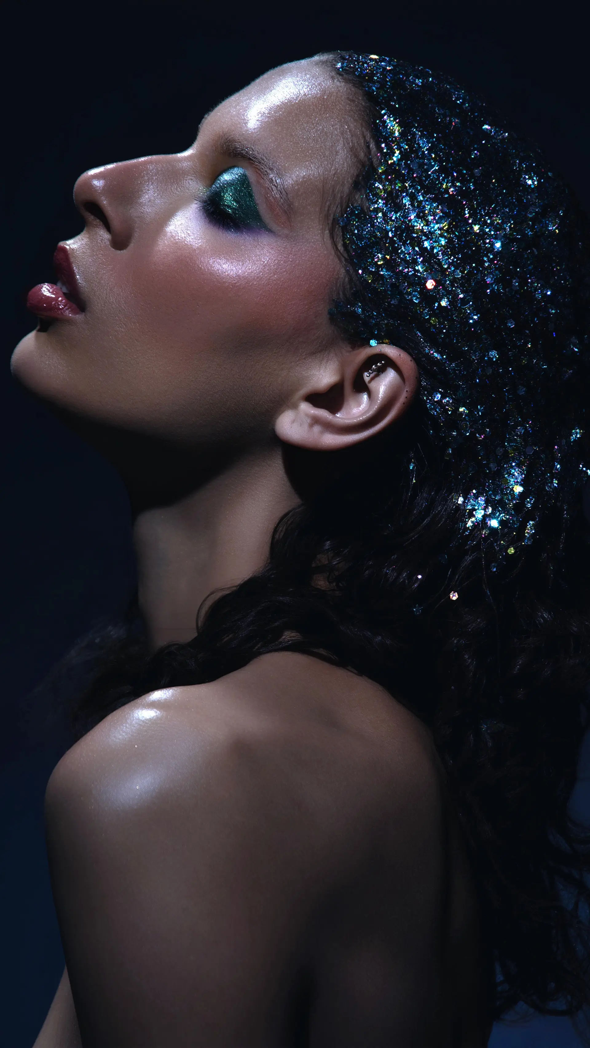 Dark wavy hair styled with an editorial wet look and heavily coated with vibrant iridescent glitter along the crown. 1