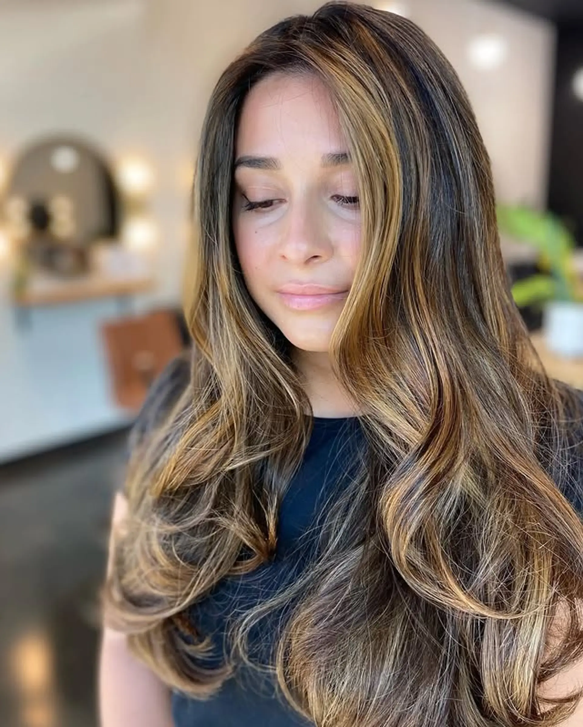 Long, wavy hair with layered caramel highlights and face-framing. 1
