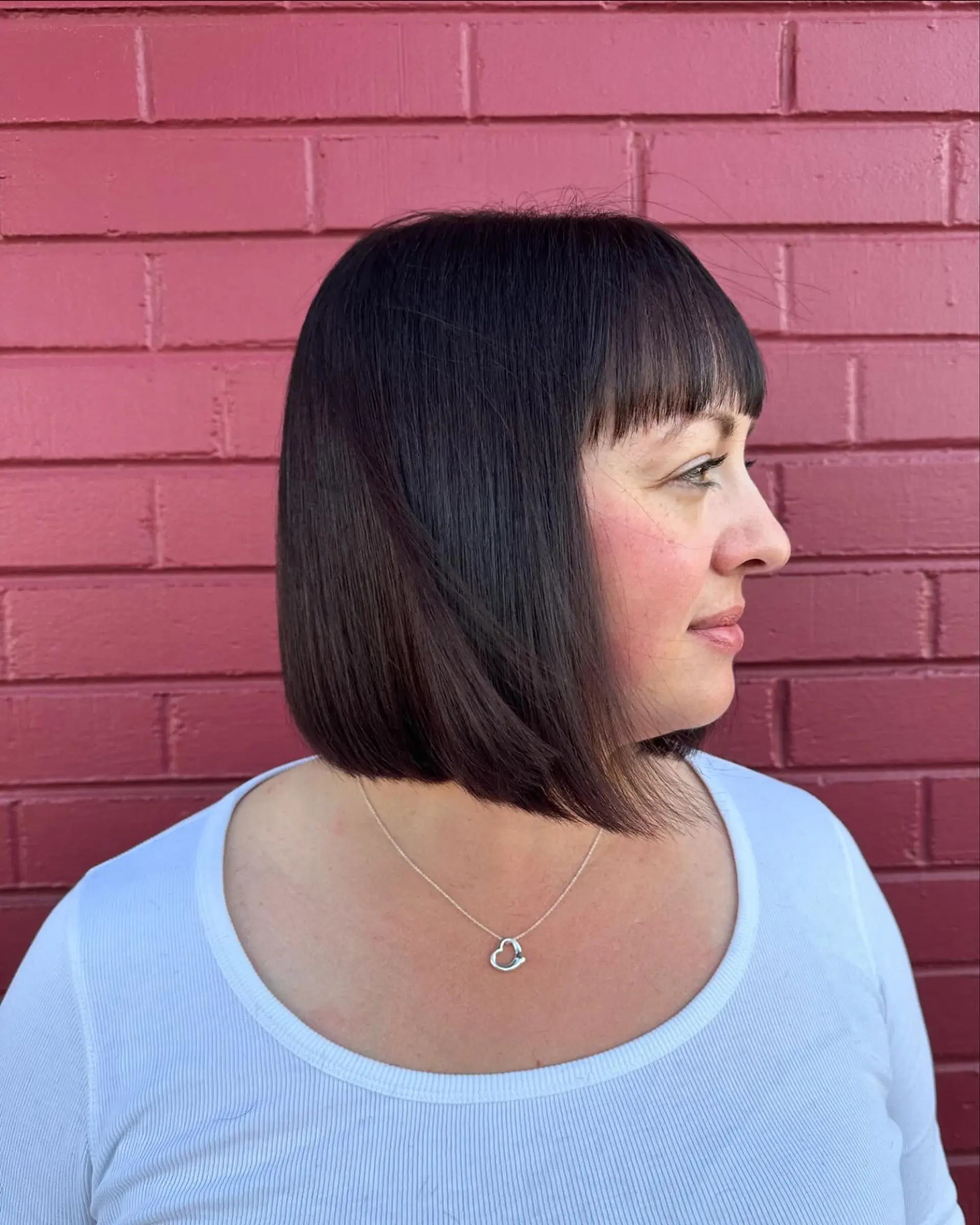 A sleek chin-length blunt bob with straight bangs in a rich deep brunette shade. 1