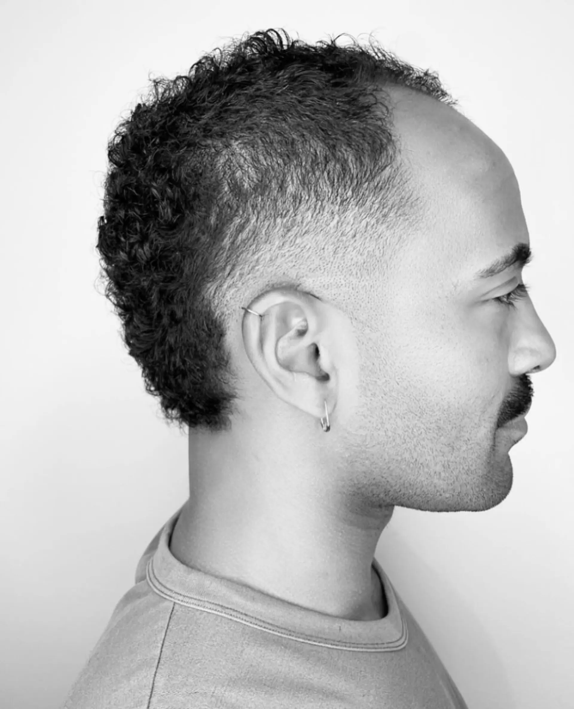 A modern curly mullet featuring clean, tapered skin-faded sides with textured natural curls along the top and down the nape. 1