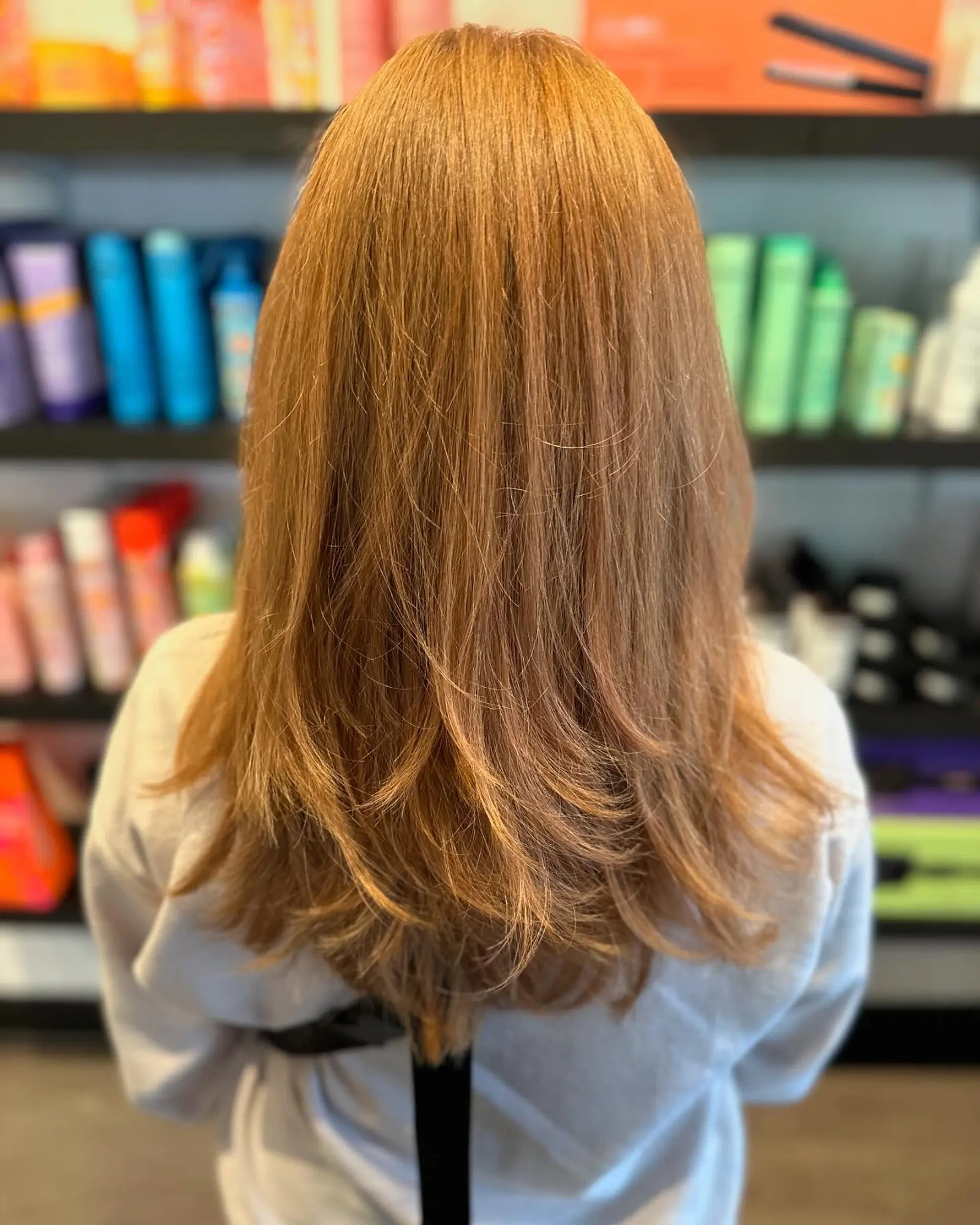 Long warm strawberry-blonde hair cut into textured butterfly layers with softly flicked ends. 1