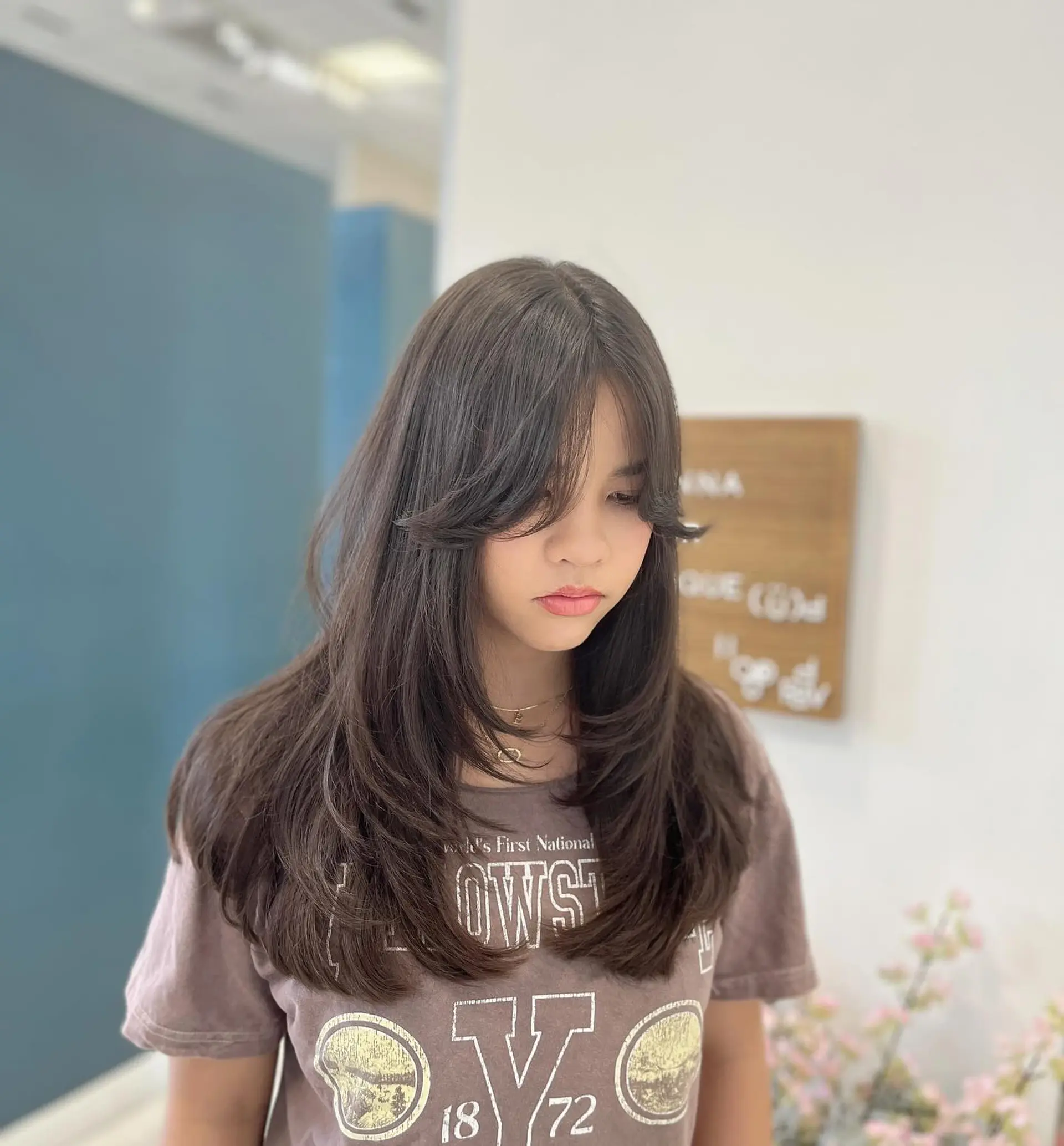 Long layered haircut featuring outward-flipped curtain bangs and soft, face-framing feathered ends. 1