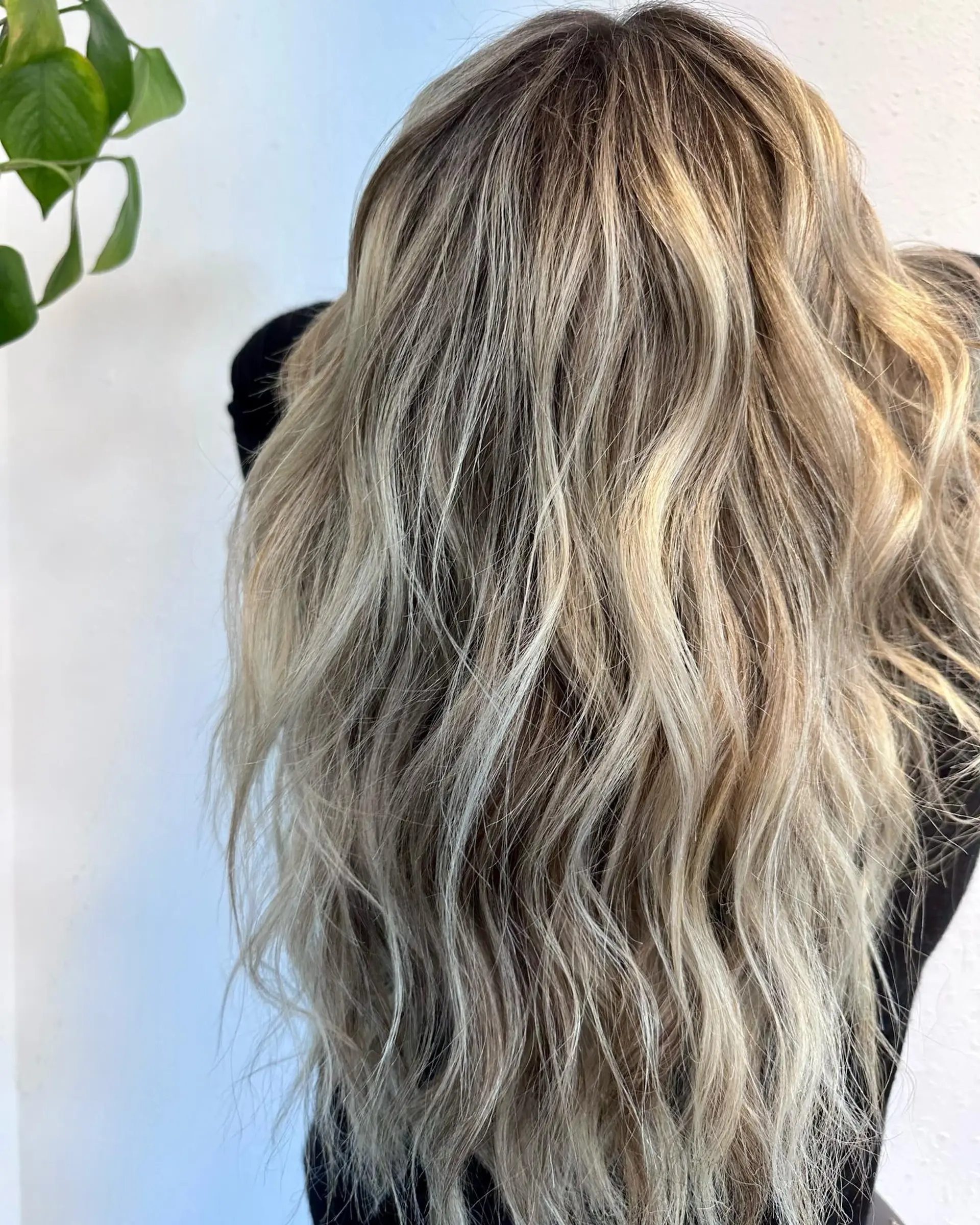 Long dimensional blonde hair blended with subtle dark root tones and styled into loose, textured waves. 1