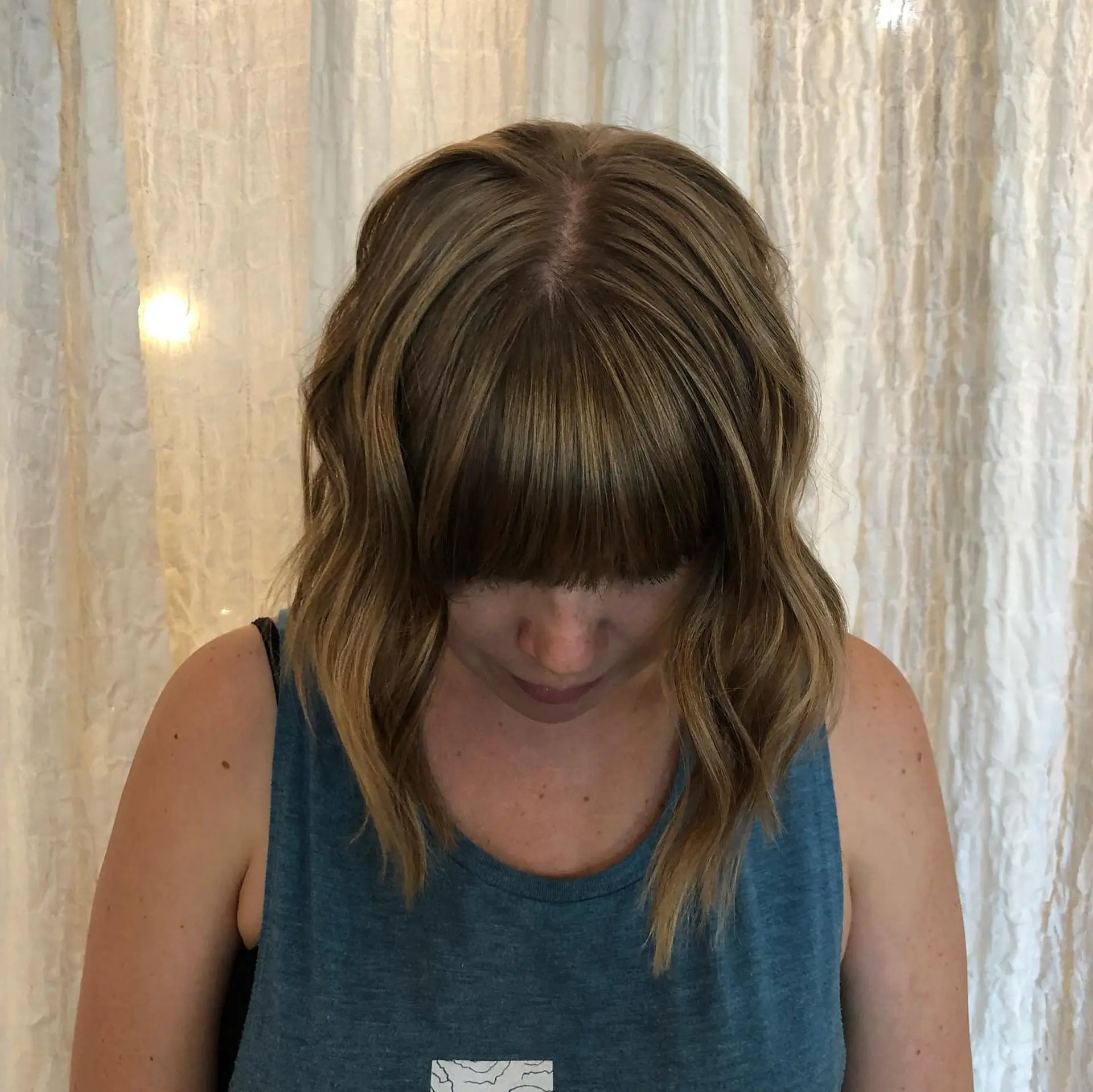 A textured, collarbone-length lob styled with loose bends and paired with a straight, full fringe. Dimensional babylights are blended seamlessly into a natural light brunette base. 1