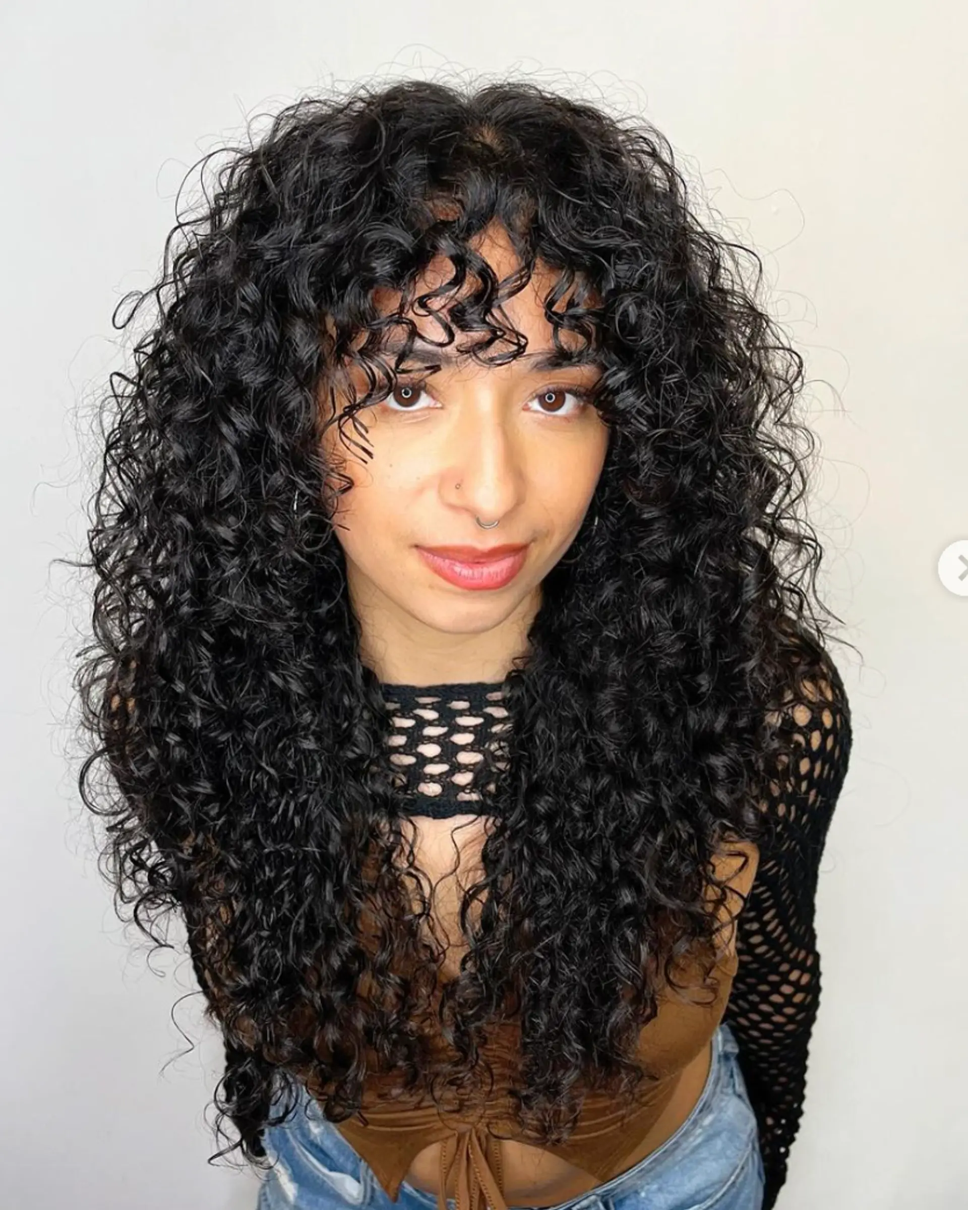 A long, curly hairstyle with voluminous black curls and curly bangs framing the face, creating a full-bodied and playful look.

Cut and style by @juliamannino_hair
 1