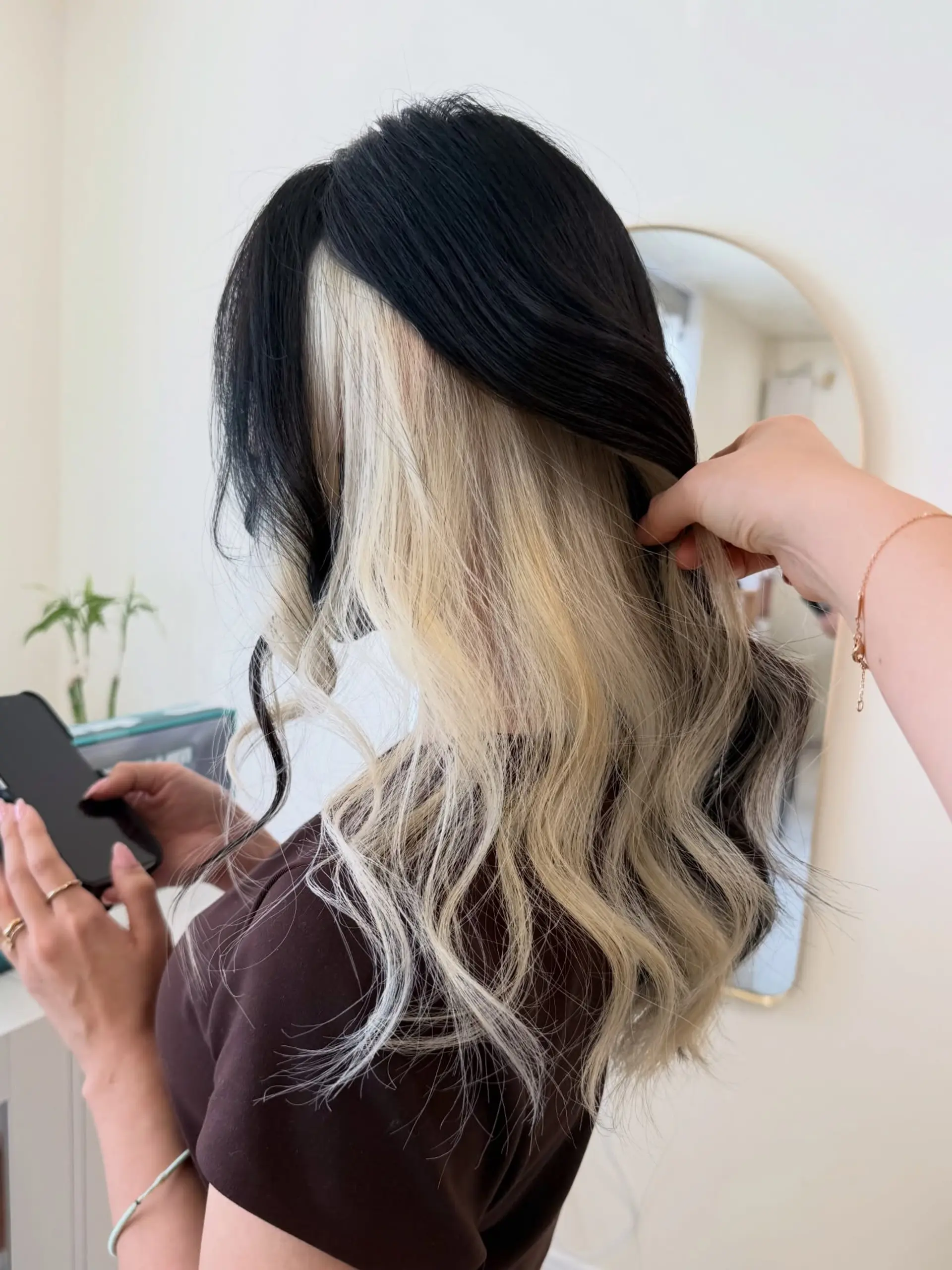 Jet black long hair styled in soft waves, parted to reveal a high-contrast platinum blonde peekaboo underlayer. 1