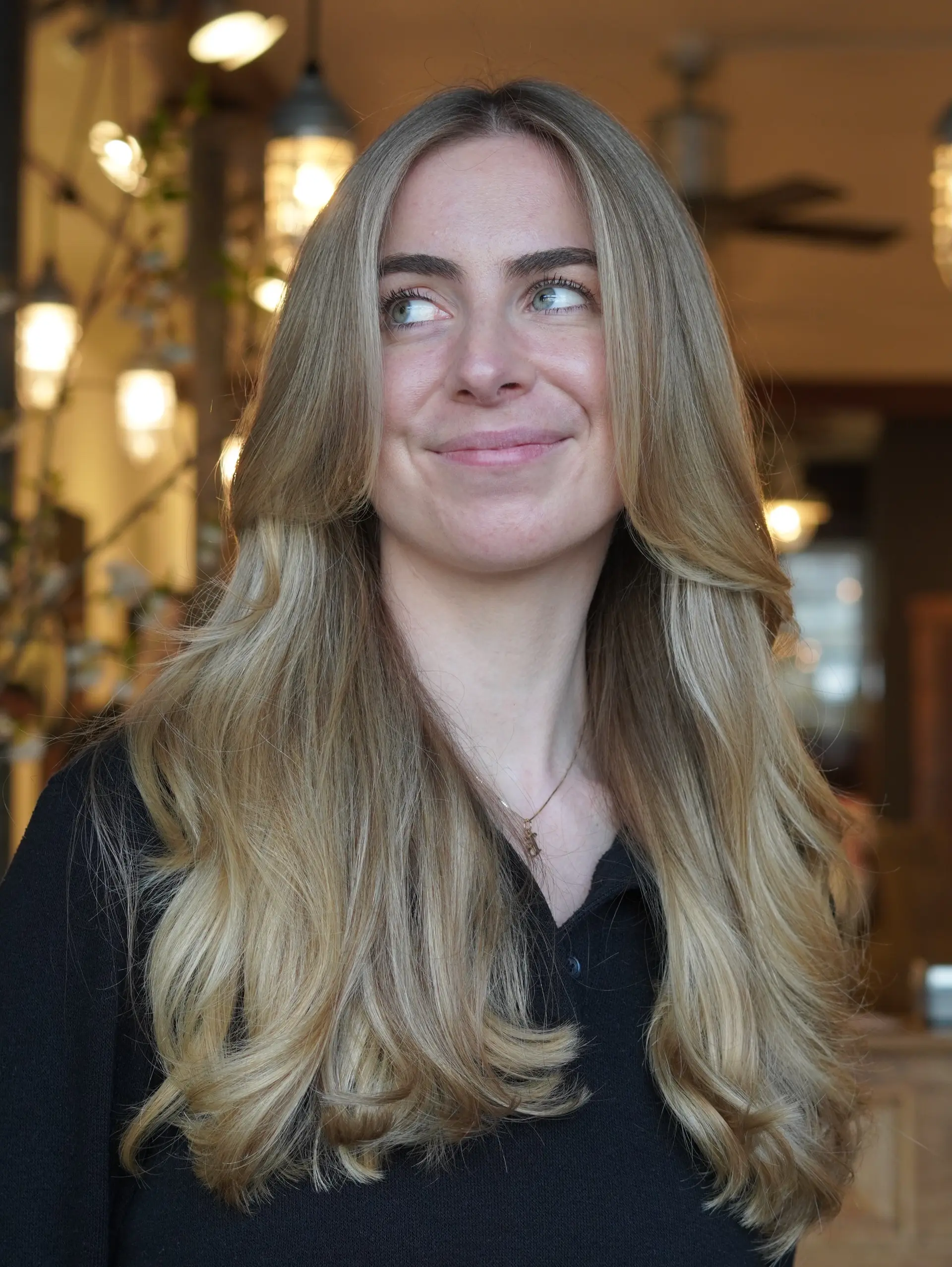 Long blonde hair styled with full dimensional highlights, long face-framing curtain bangs, and soft wavy blowout curls. 1