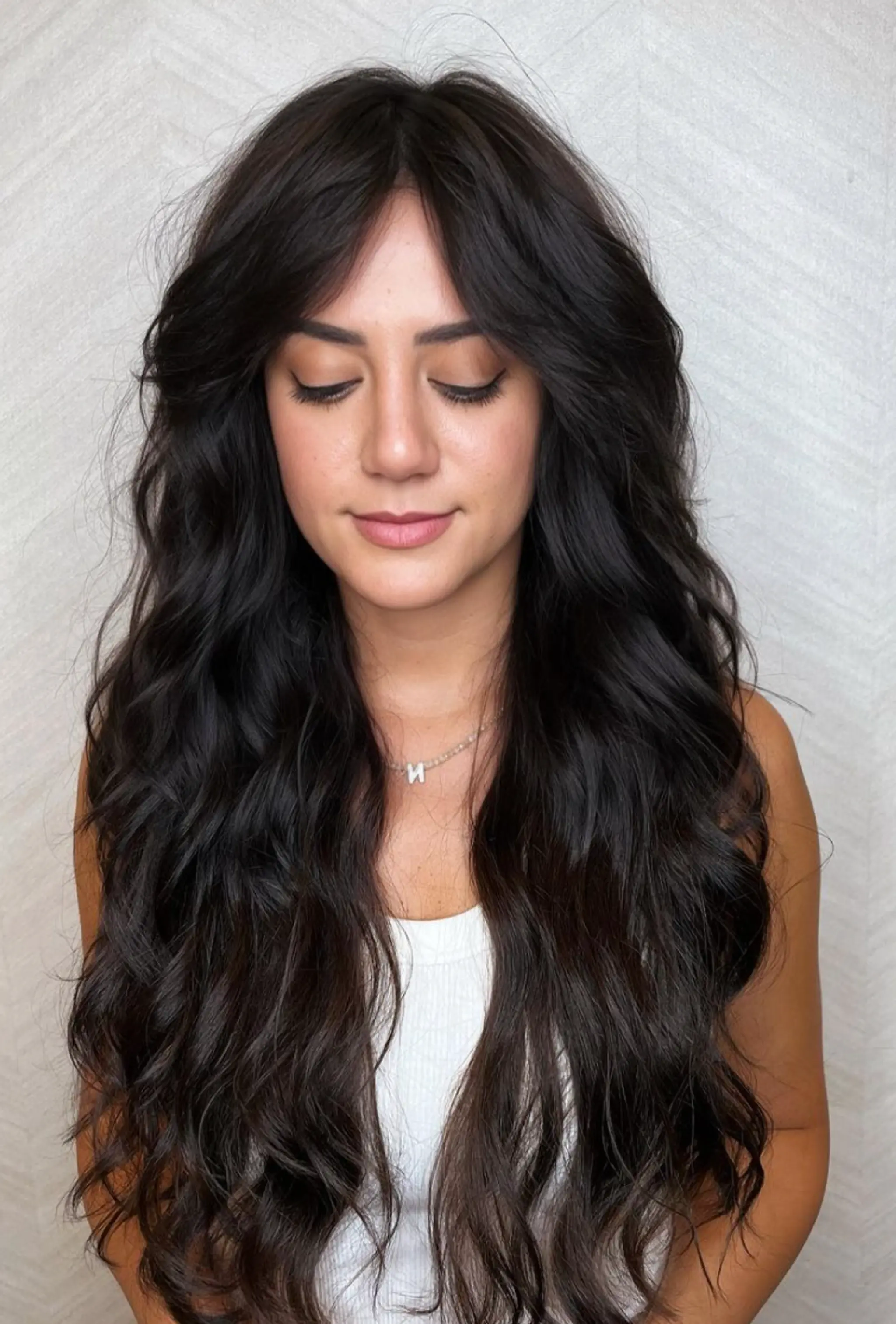 A voluminous style featuring very long wavy black hair with natural shine, curtain bangs, and intricate layers.

Cut and style by @juliamannino_hair

